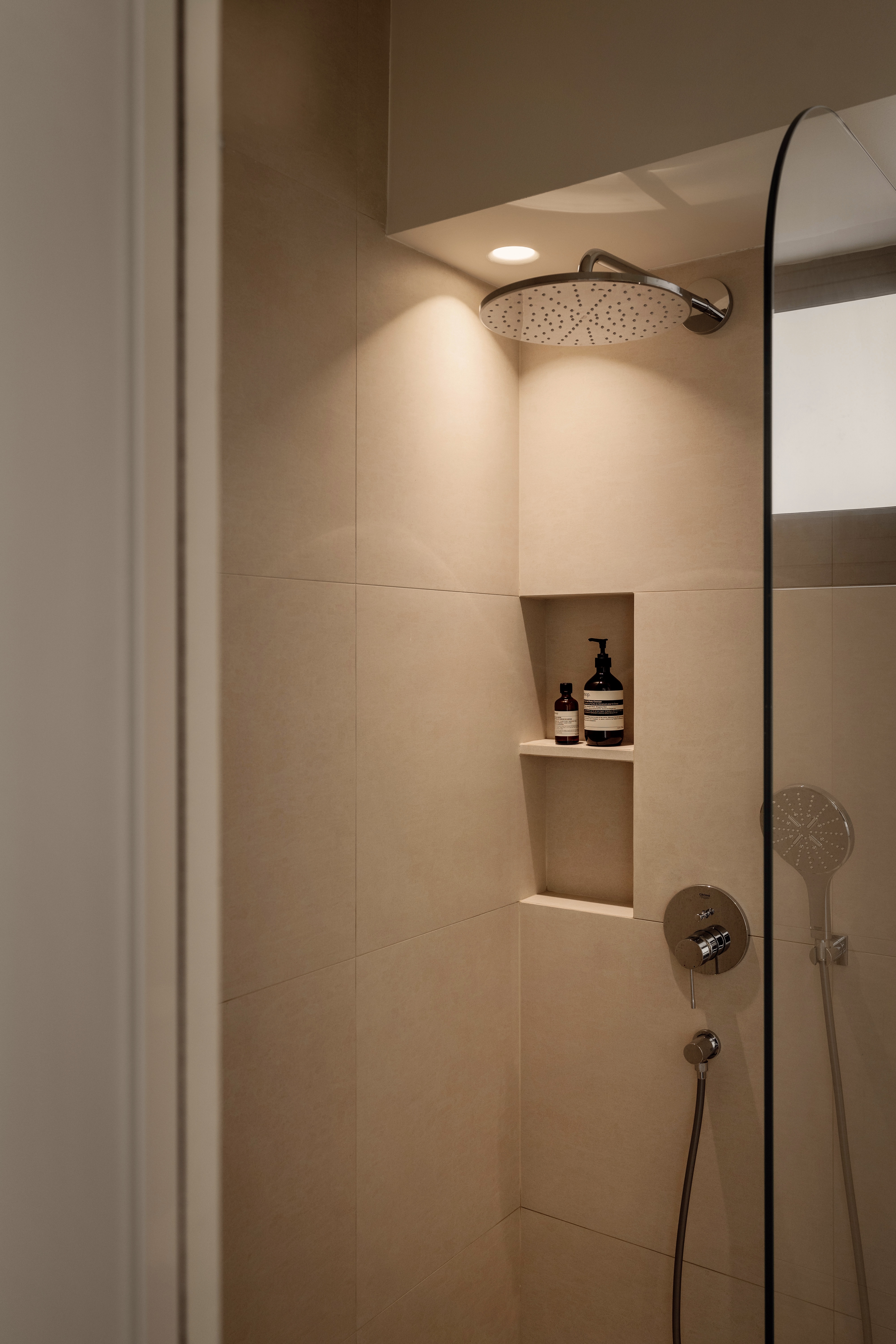 A Creamy Home With Sunrise View  - Modern minimalist bathroom, beige tiles, sleek showerhead, built-in shelf, toiletries