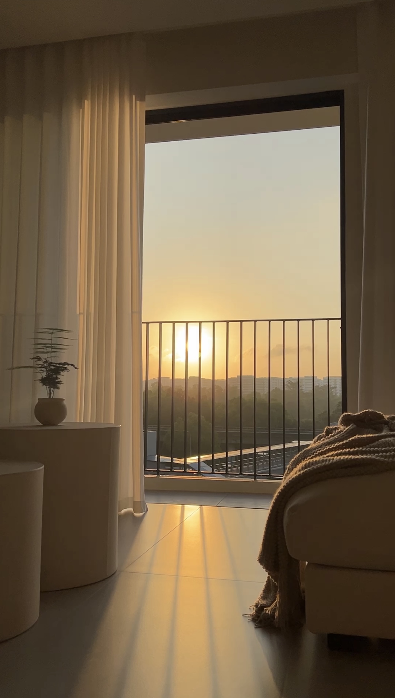 A Creamy Home With Sunrise View  - Sunset view from balcony, soft golden light, cityscape in the distance, warm indoor