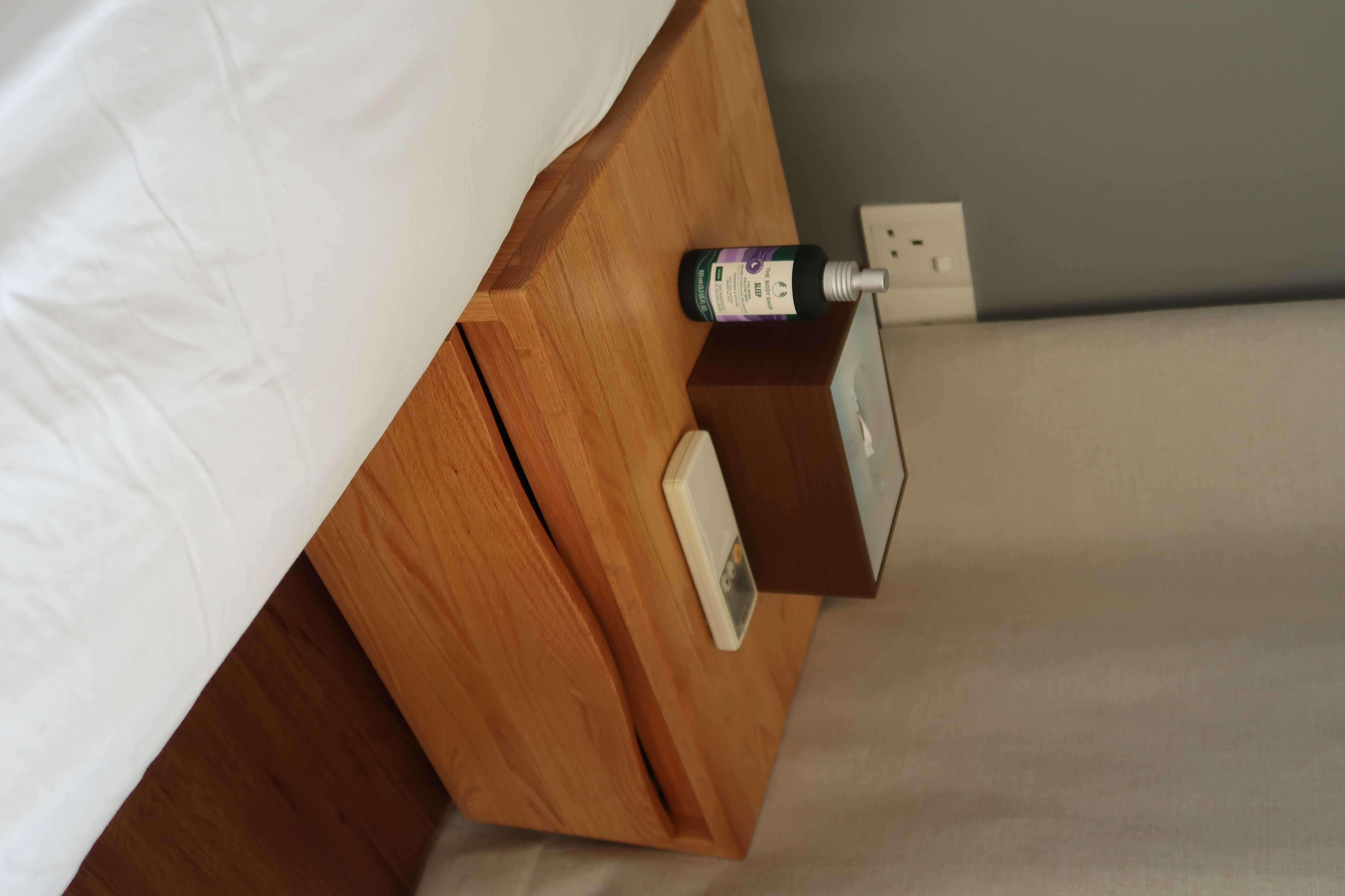 Minimal Bedroom: Our place to unwind and relax  - Wooden nightstand, white bed sheets, wooden drawer, white wall outlet