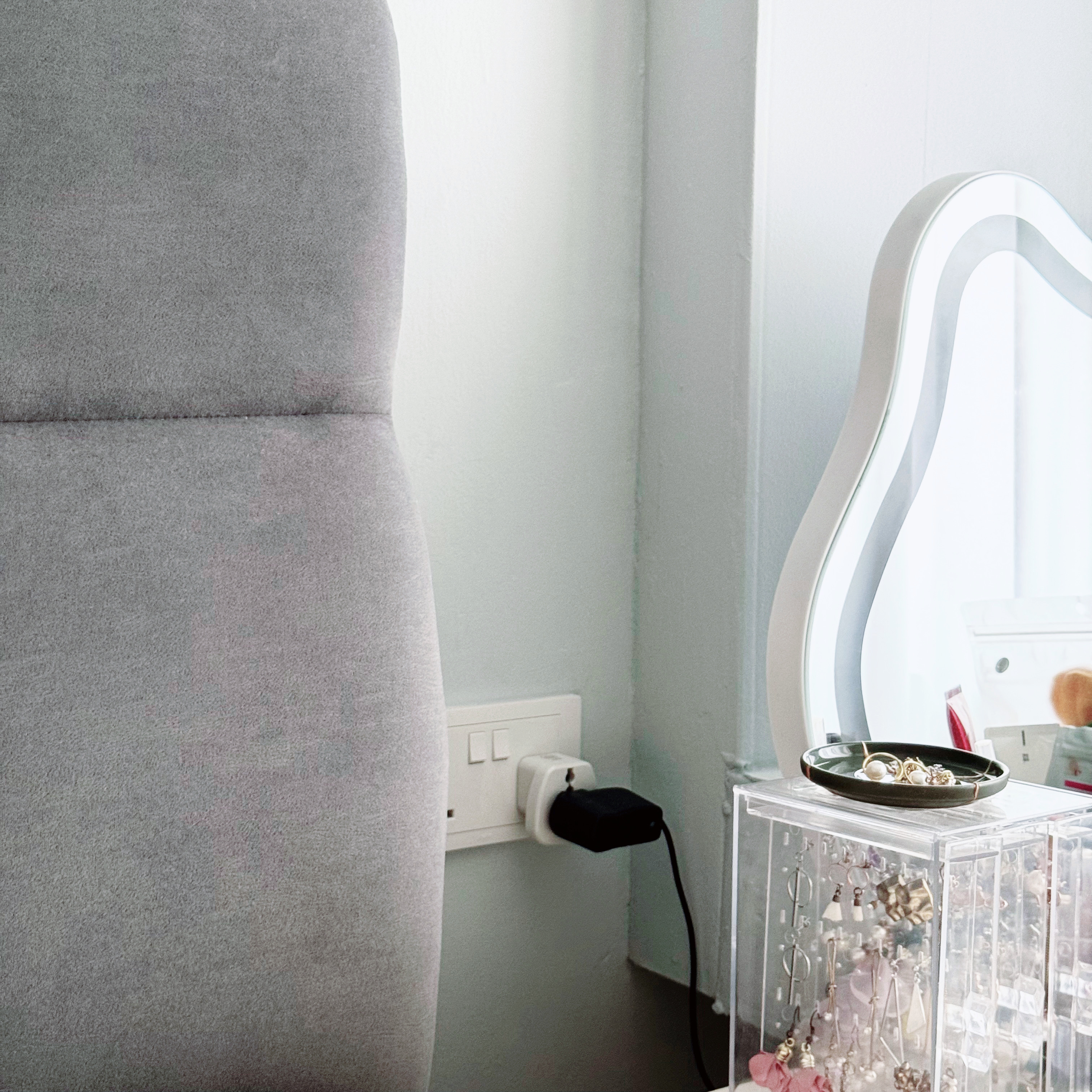 Peek into the tofus' recharging station! 💤  - Grey upholstered chair, white wall, modern design, soft lighting, minimalist