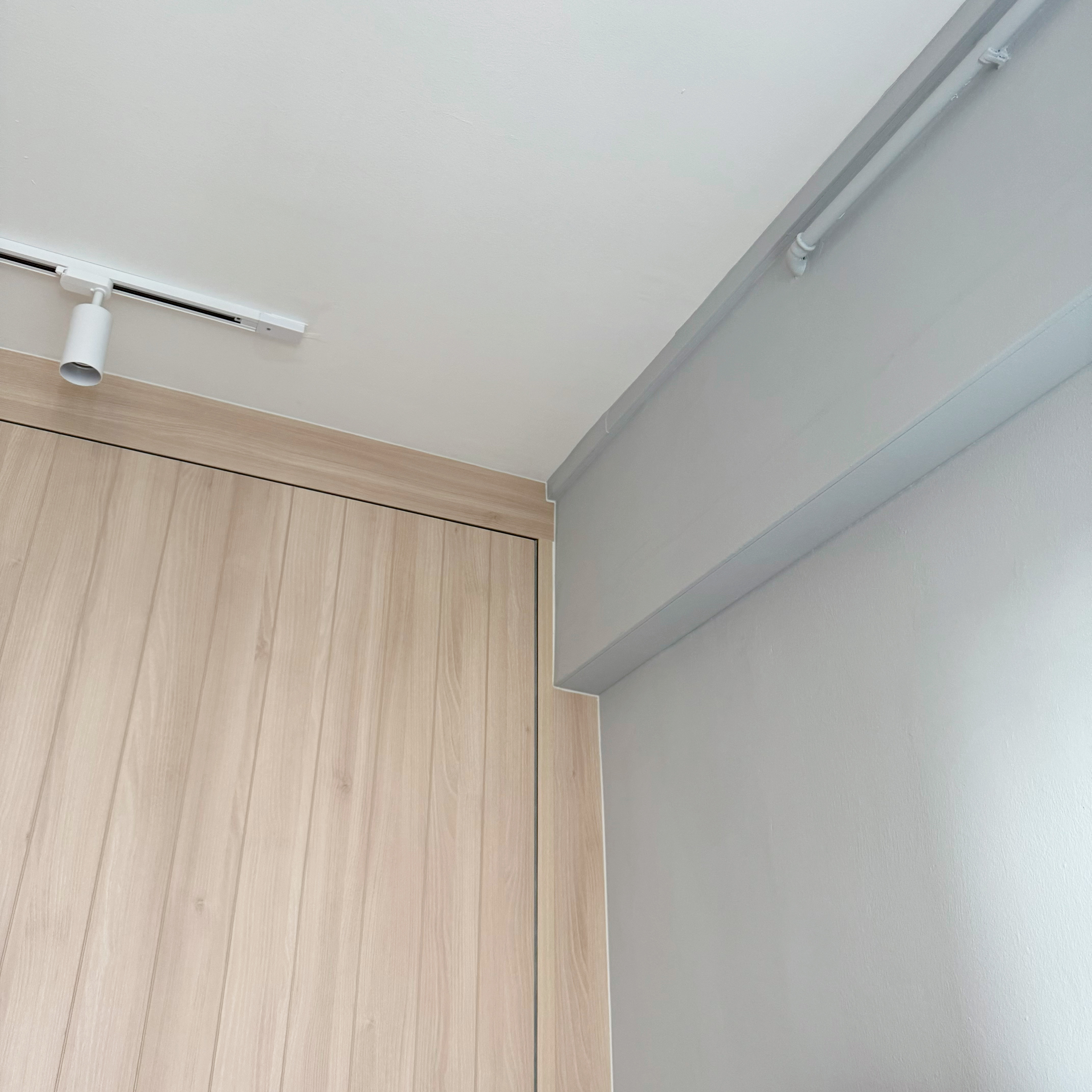 Peek into the tofus' recharging station! 💤  - Light wood door, white ceiling, gray wall, recessed lighting, white track