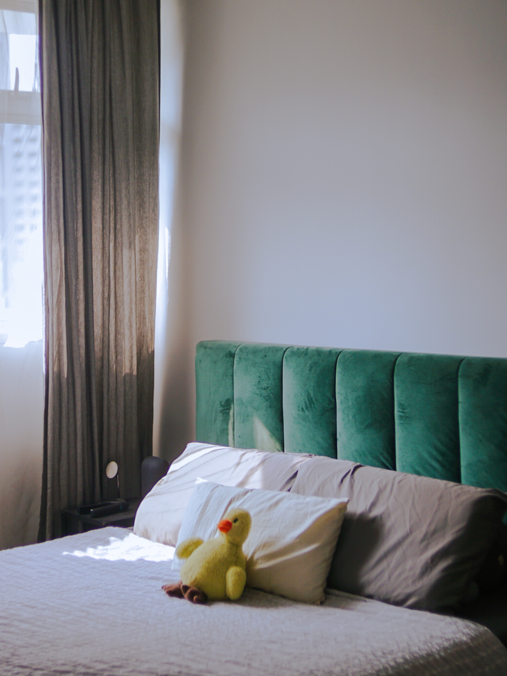 Our Bedroom With No Built-In Cabinets - Green upholstered headboard, beige pillows, yellow plush toy, white bedspread, sheer