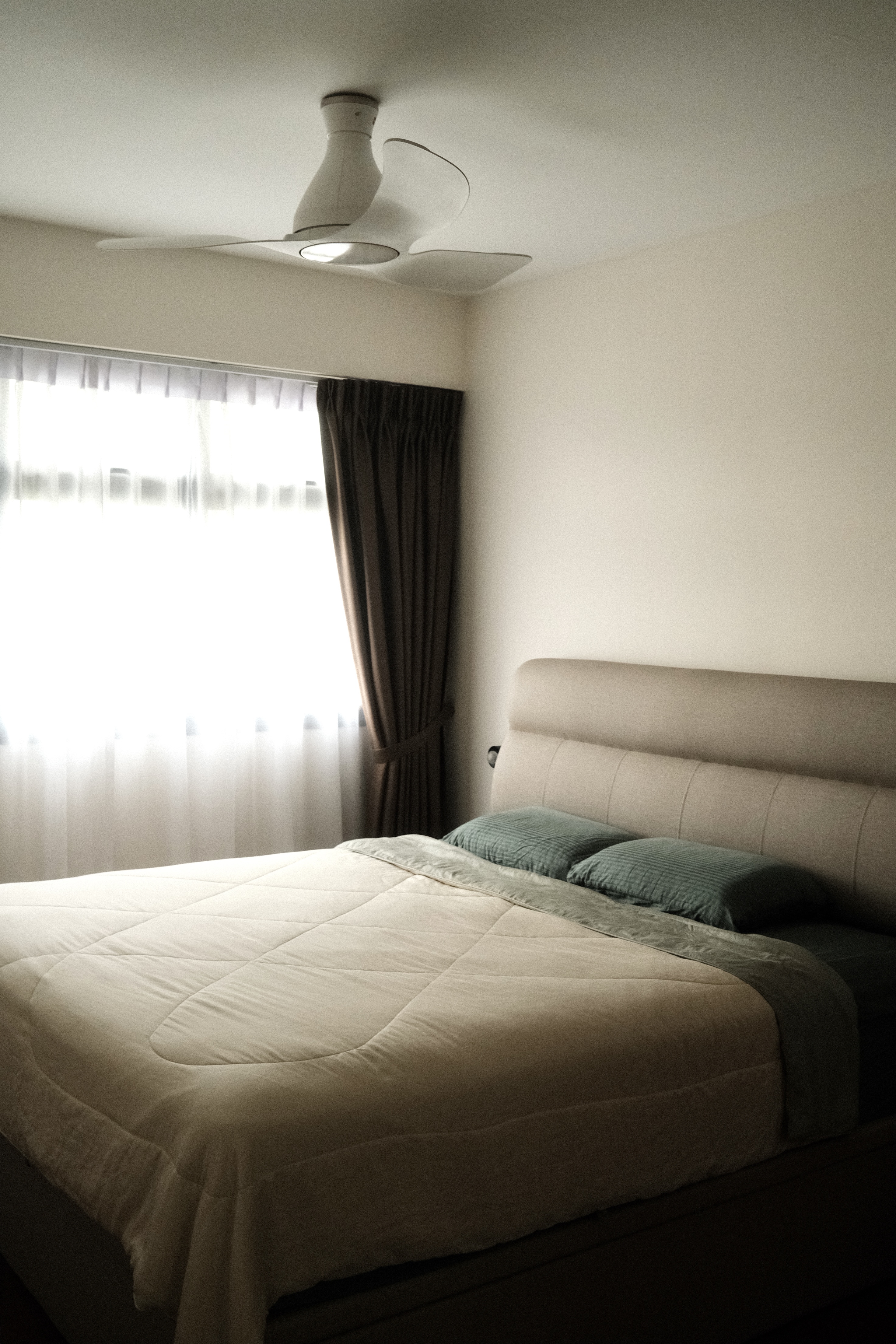 Our serene bedroom with minimal carpentry - Sunlit bedroom with modern ceiling fan, beige upholstered headboard, neatly made