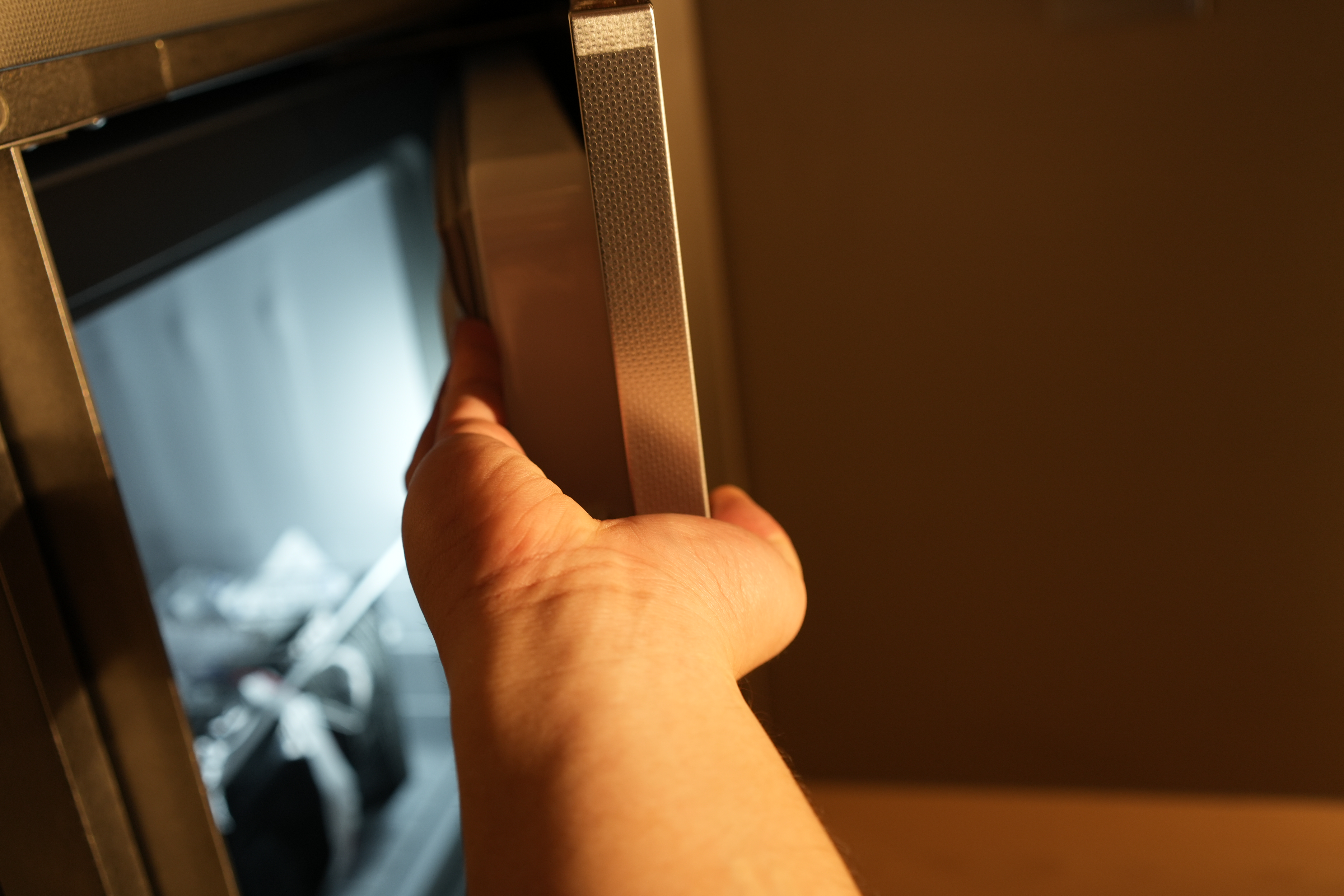 A Chef's Kitchen: Stainless Steel & Japanese Monotonal Design - Close-up of a hand opening a stainless steel microwave door