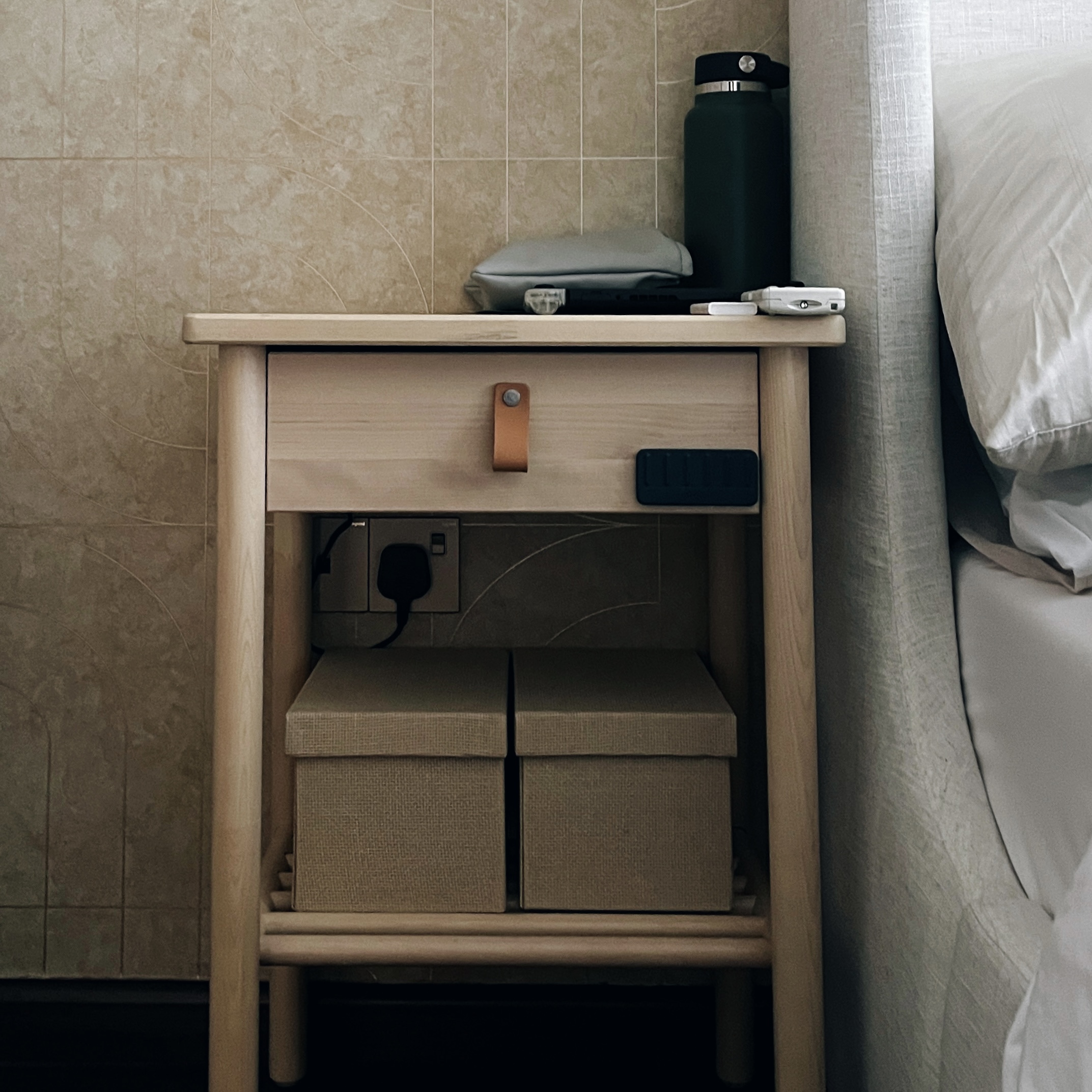 Keeping our bedroom warm and cozy! - Wooden nightstand, beige tiled wall, bedside table, black water bottle, gray pillow