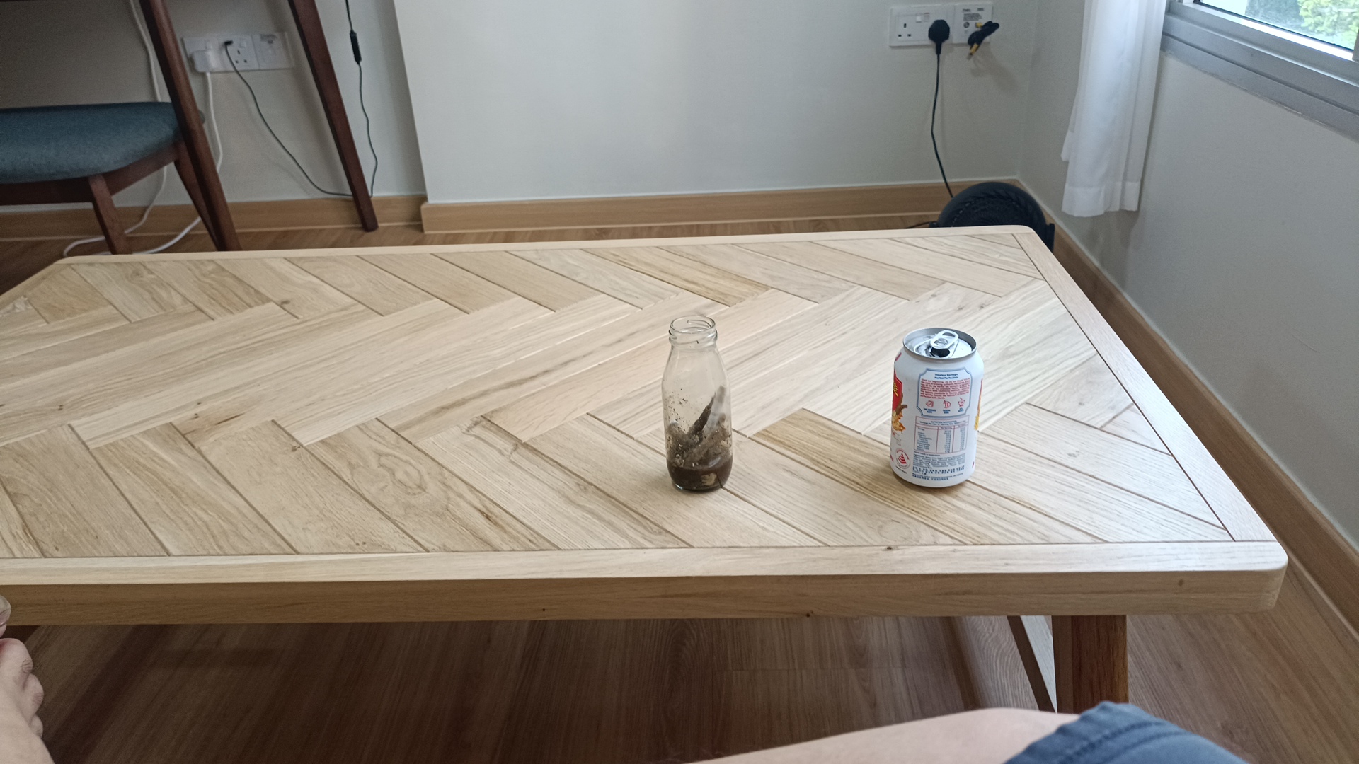 Minimalist Botak House - Wooden herringbone table, empty glass bottle, dark liquid, beverage can, indoor setting, natural