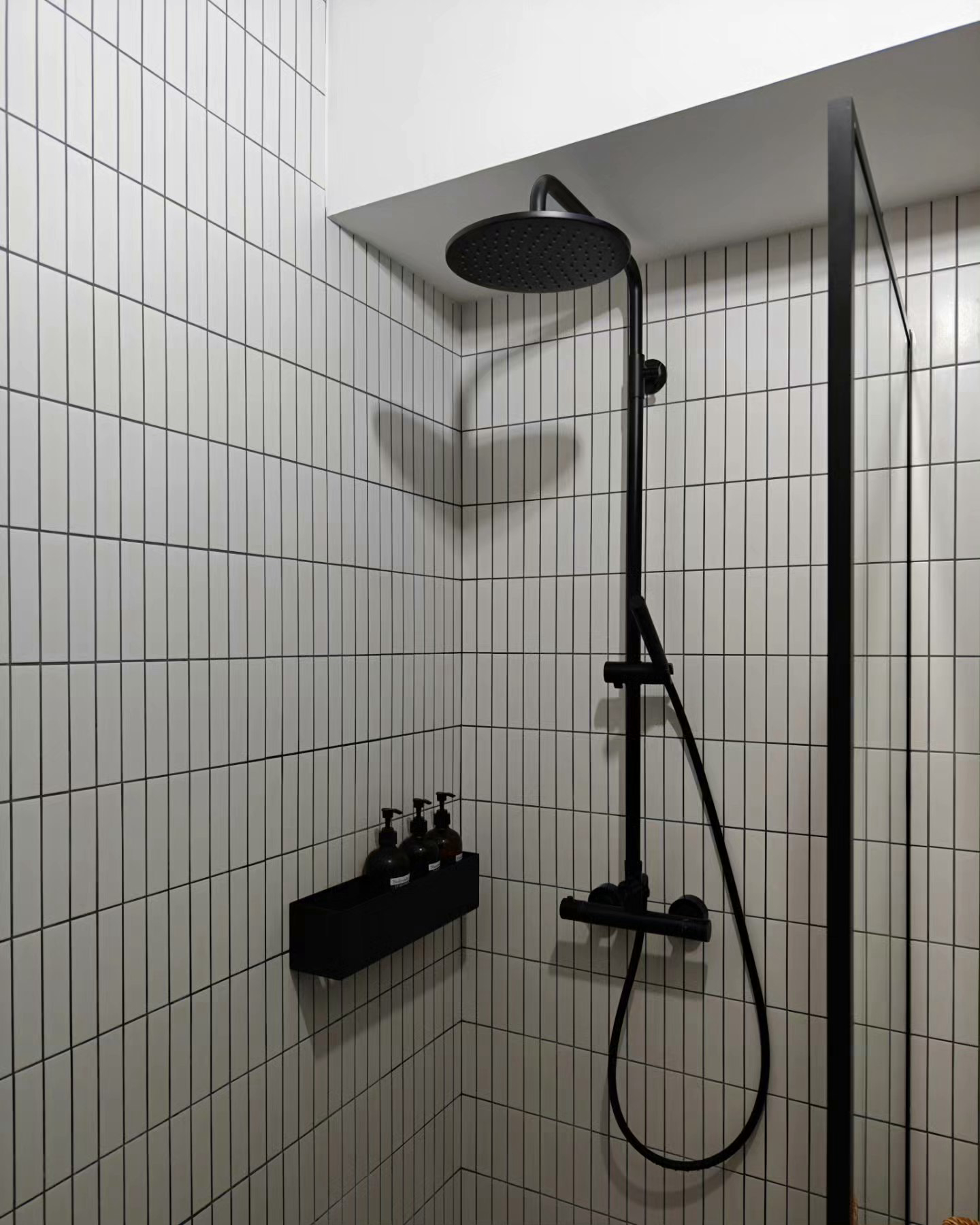 "Oh You Have 3 Bathrooms?!" - White tiled walls, black showerhead, black shower arm, black soap dispensers, black shelf