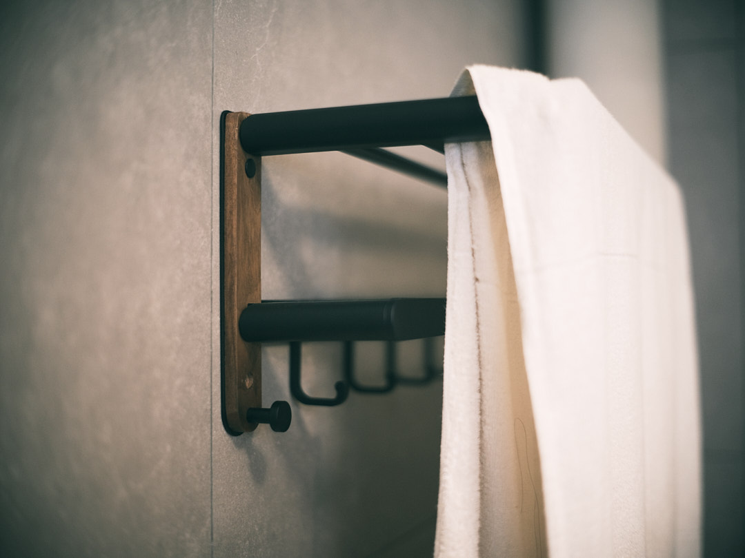 The Spa Within a Cave (Bathroom 2/3) - Wooden towel rack, black metal frame, white towel, soft lighting, modern design