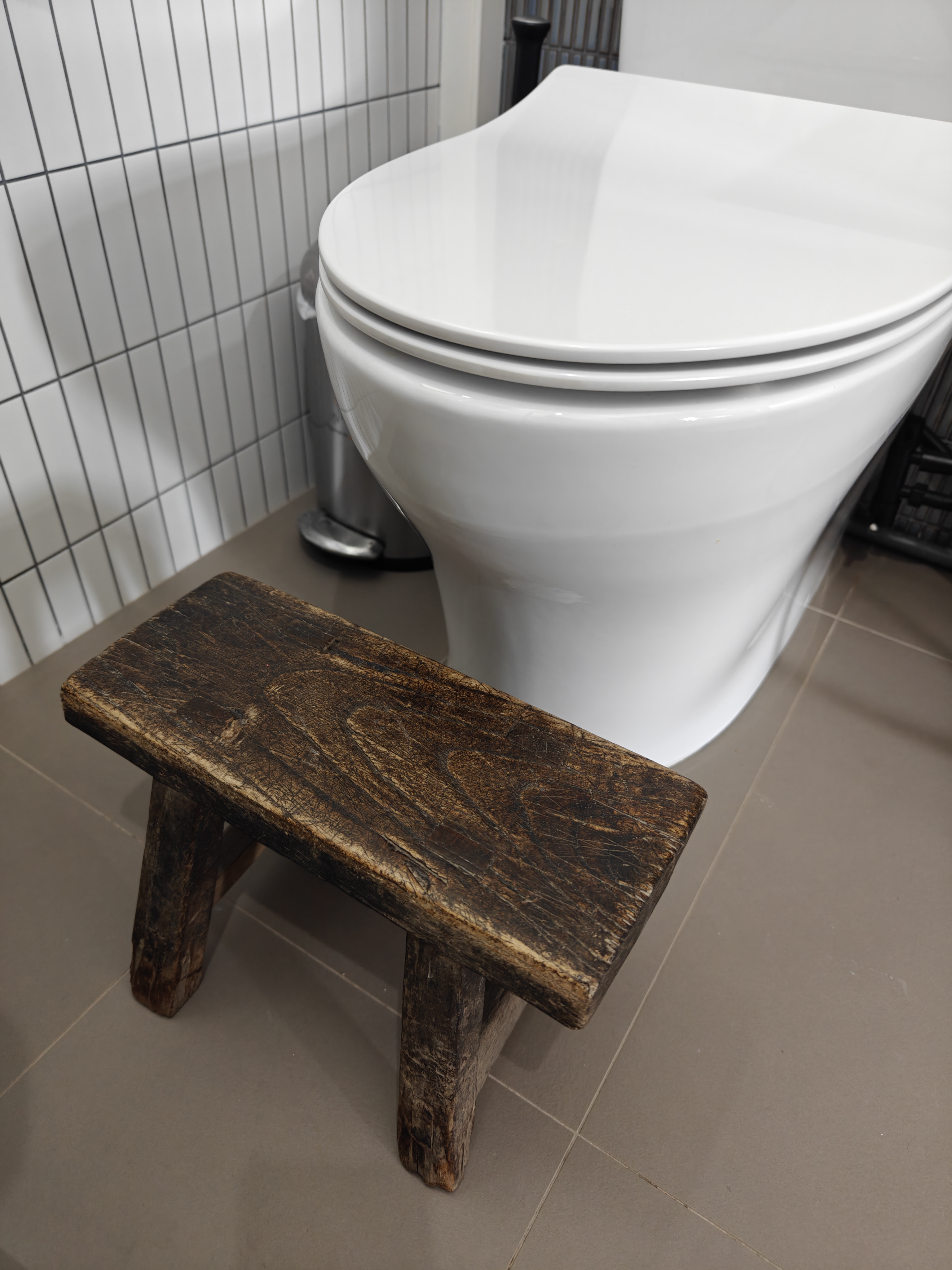 "Oh You Have 3 Bathrooms?!" - White toilet, wooden bench, rustic design, tiled floor, modern bathroom, clean lines