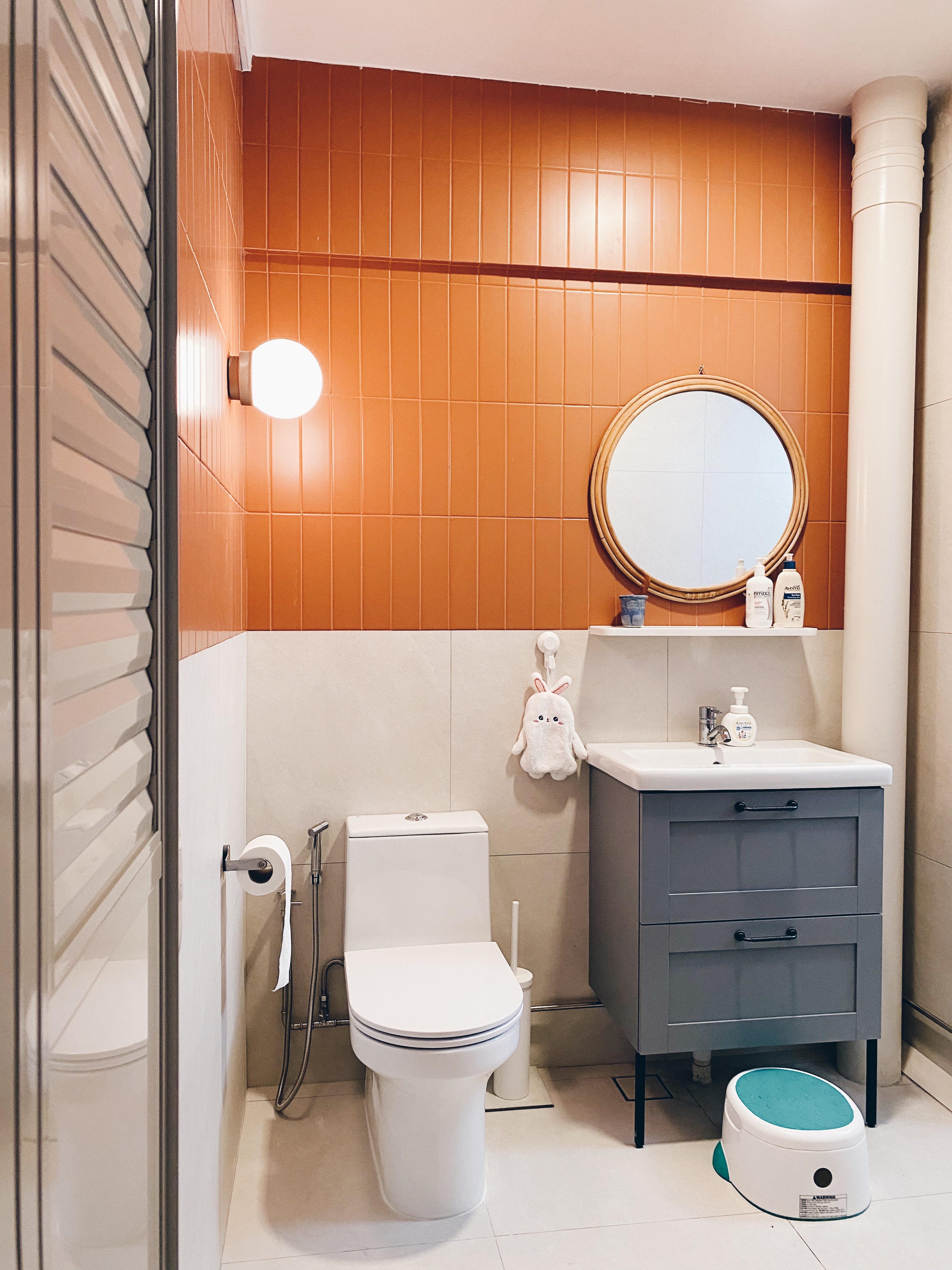 Our Bathrooms and their Personalities - Modern bathroom with orange tiles, white toilet, gray vanity, round mirror, white