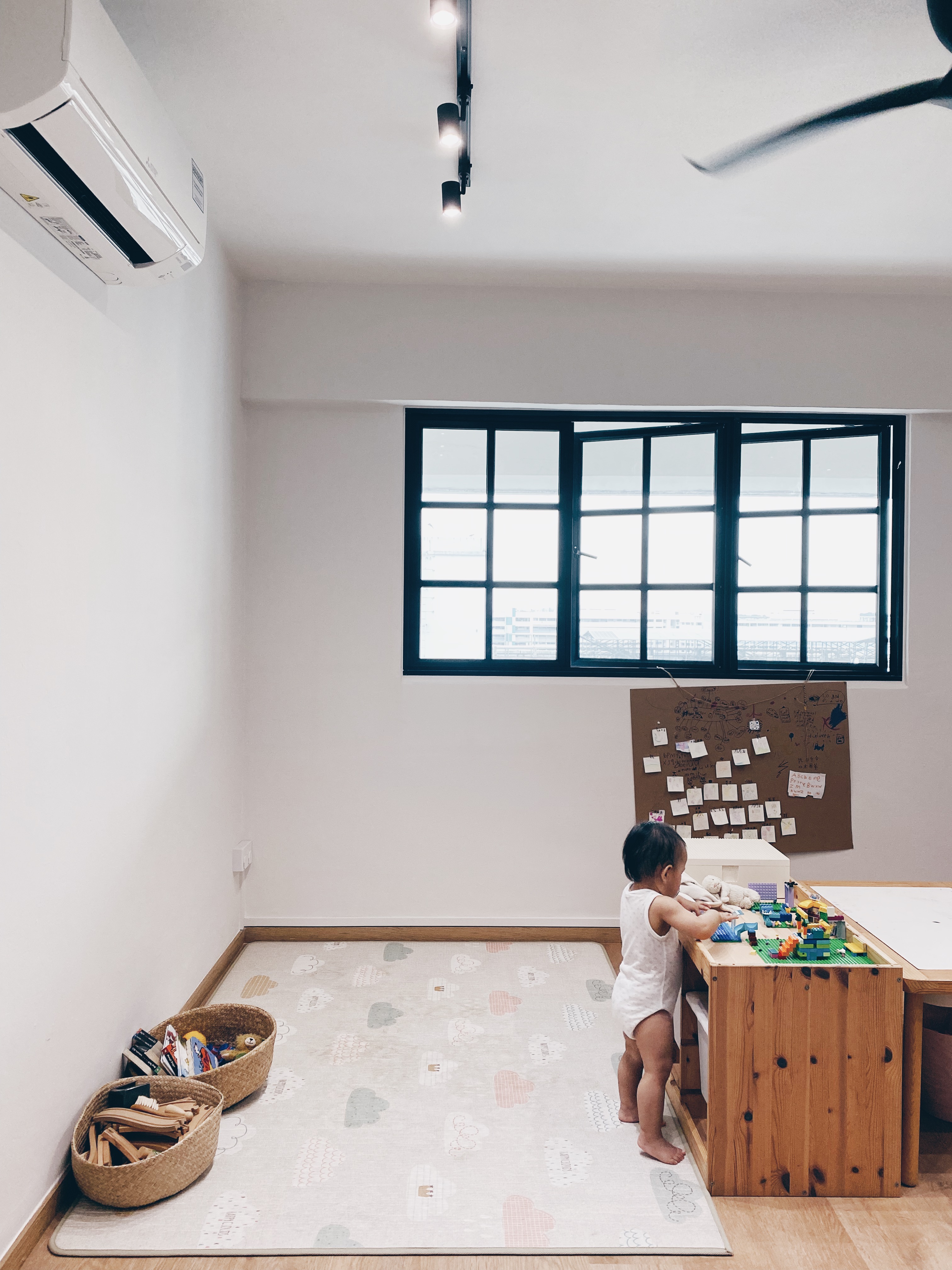 Cohabiting: working and playing together - child playing with toys, room with large windows, white walls, wooden furniture