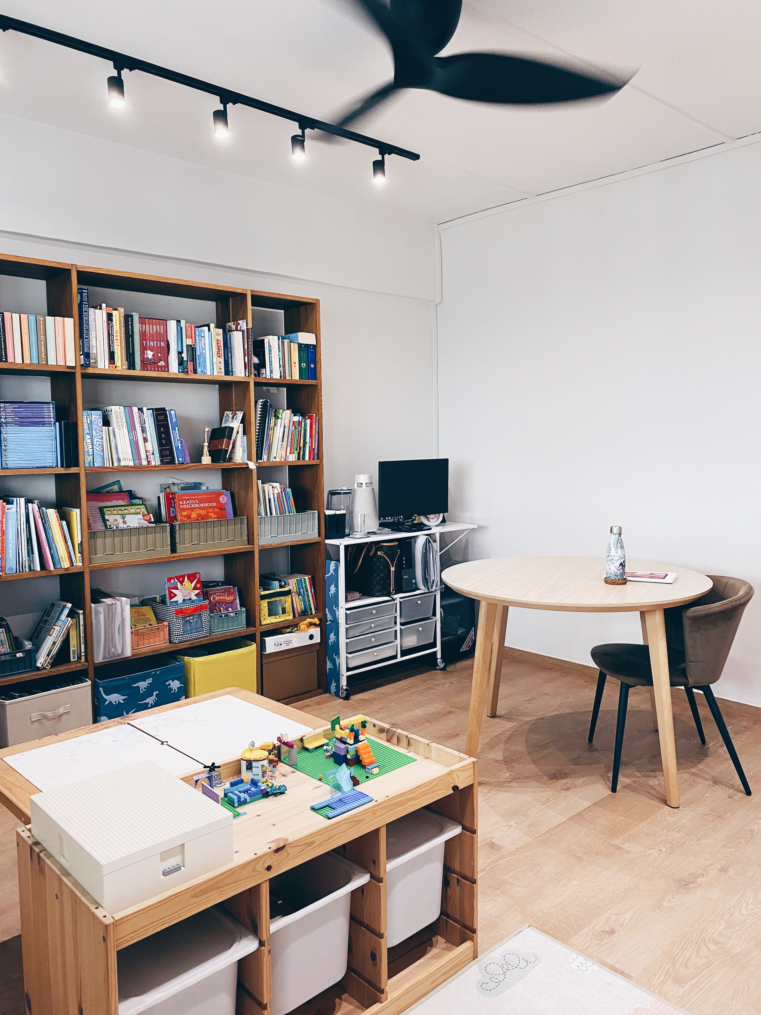 Cohabiting: working and playing together - Wooden bookshelf filled with books, children's books, and toys, ceiling fan with