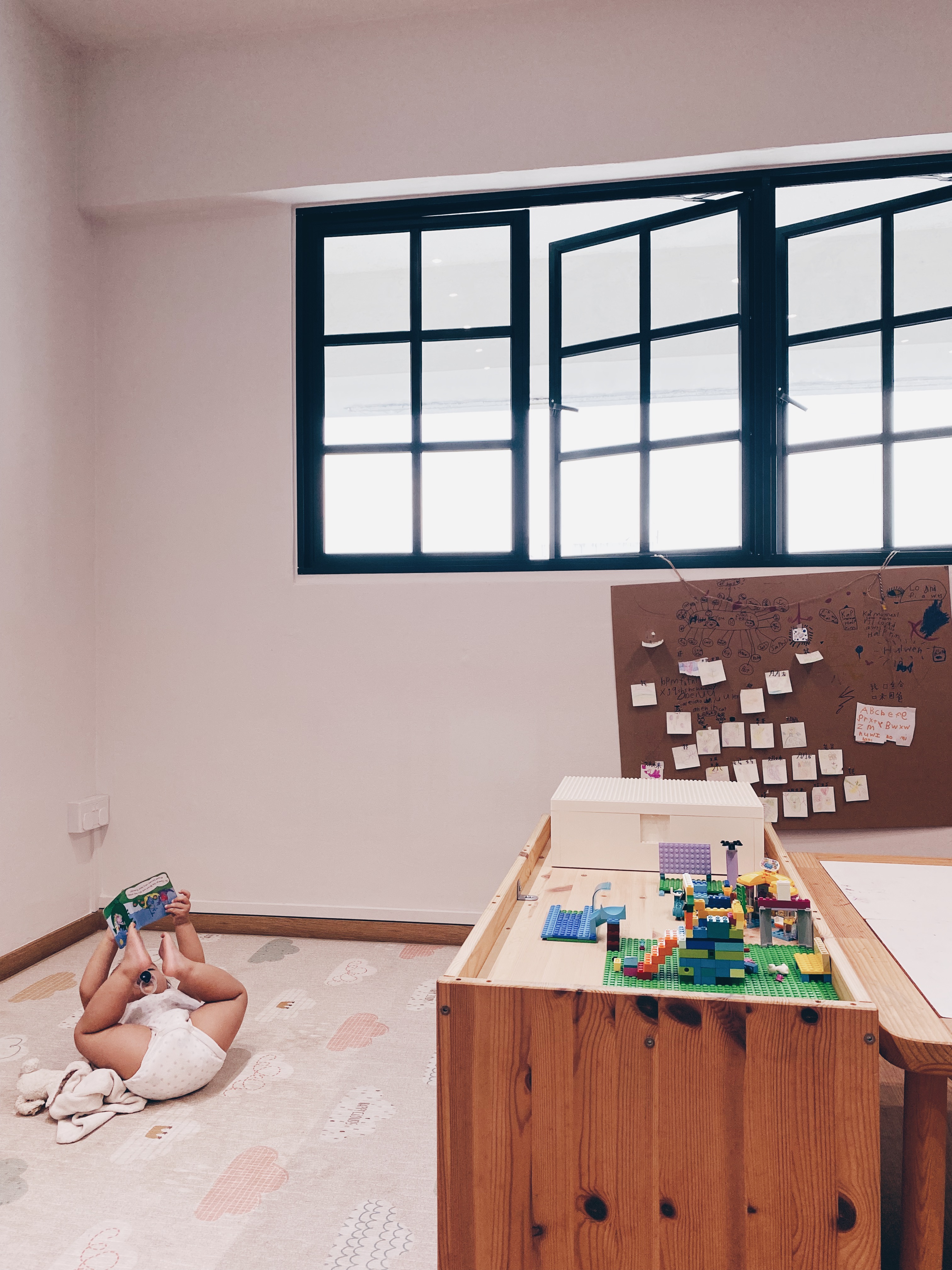 Cohabiting: working and playing together - child lying on floor, reading book, colorful blocks, wooden table, white blanket