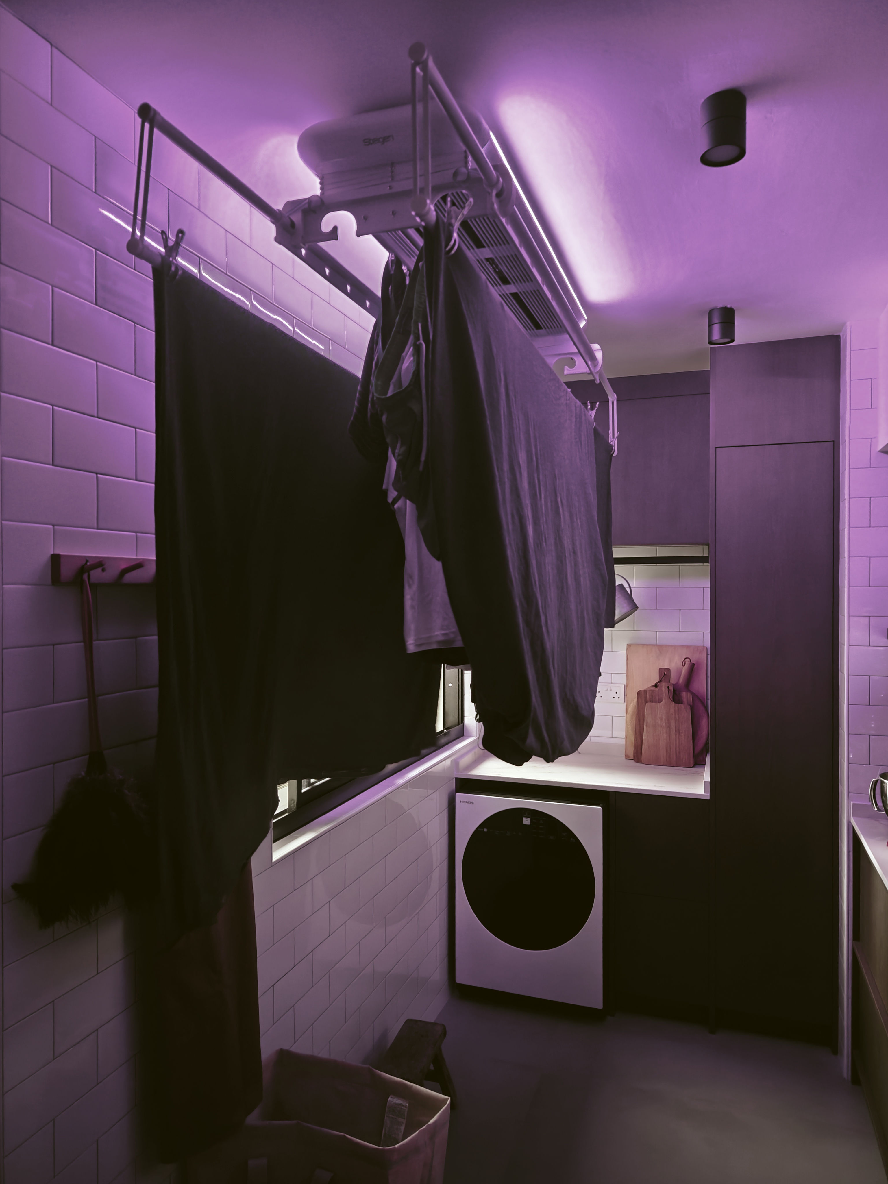 A Laundry Area Within A Kitchen - Purple-tinted bathroom, hanging clothes, tiled walls, laundry basket, dark clothing, black