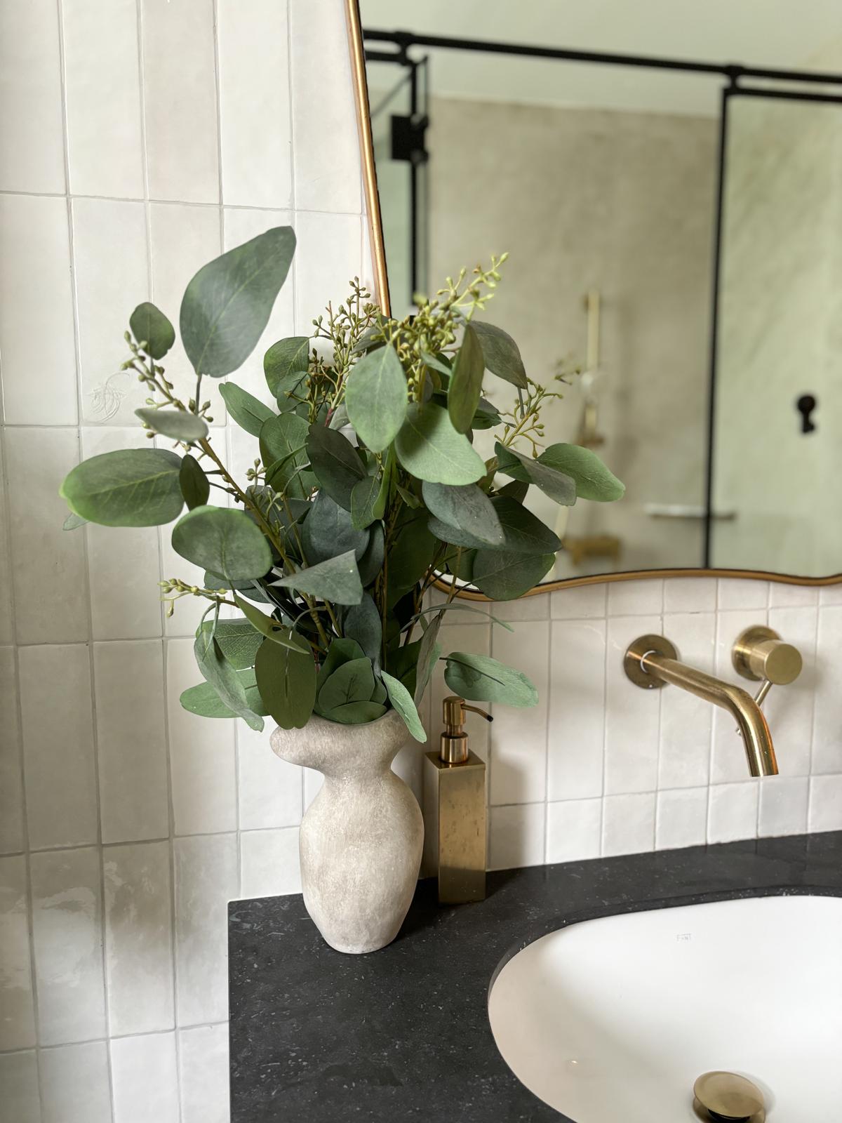 Black and white bathroom with lots of natural lighting  - vase with green leaves, bathroom vanity, white tiles, mirror, gold
