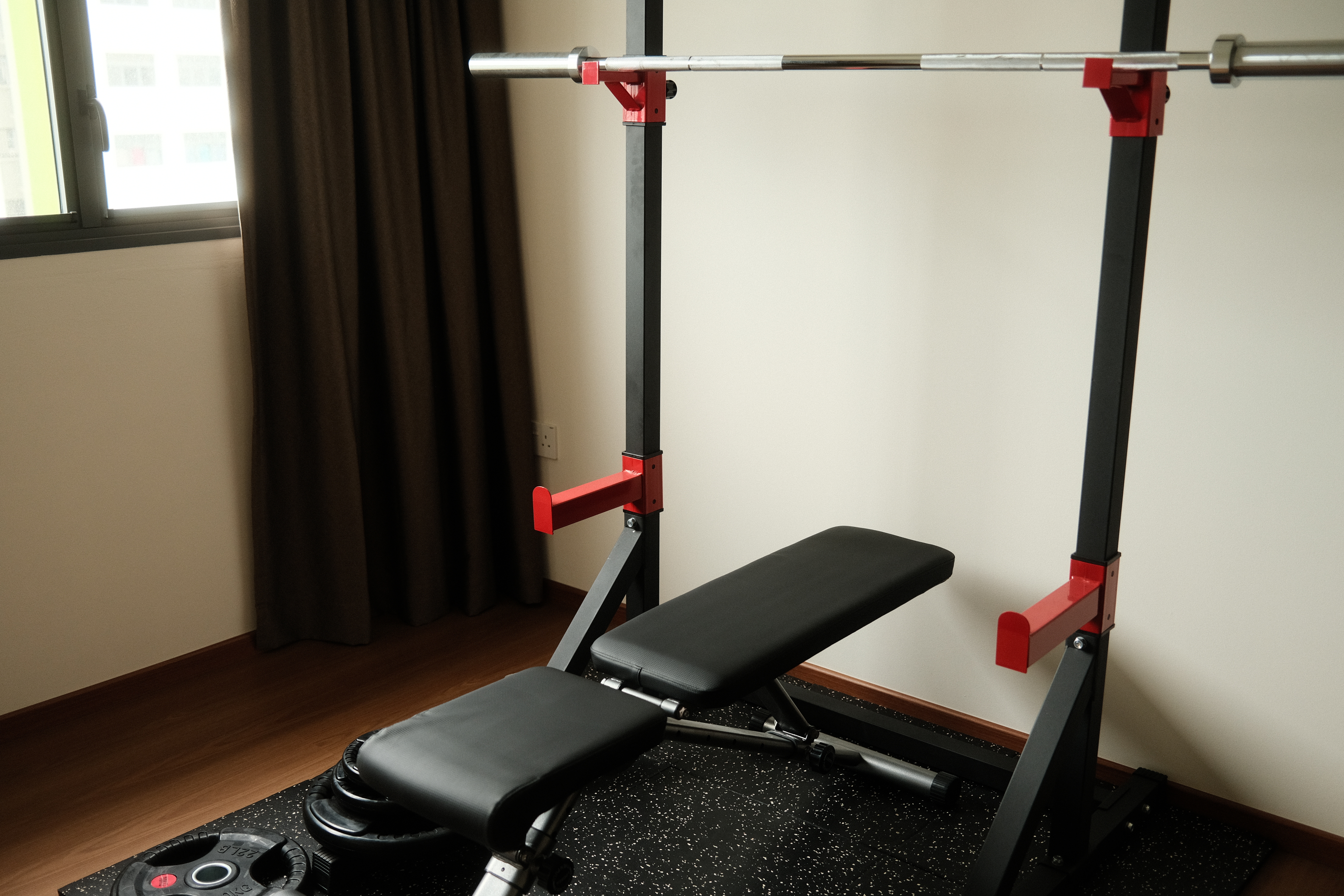 Trying to be healthy in our home gym - Black bench press, black cushioned seat, red adjustable bar, black and red exercise
