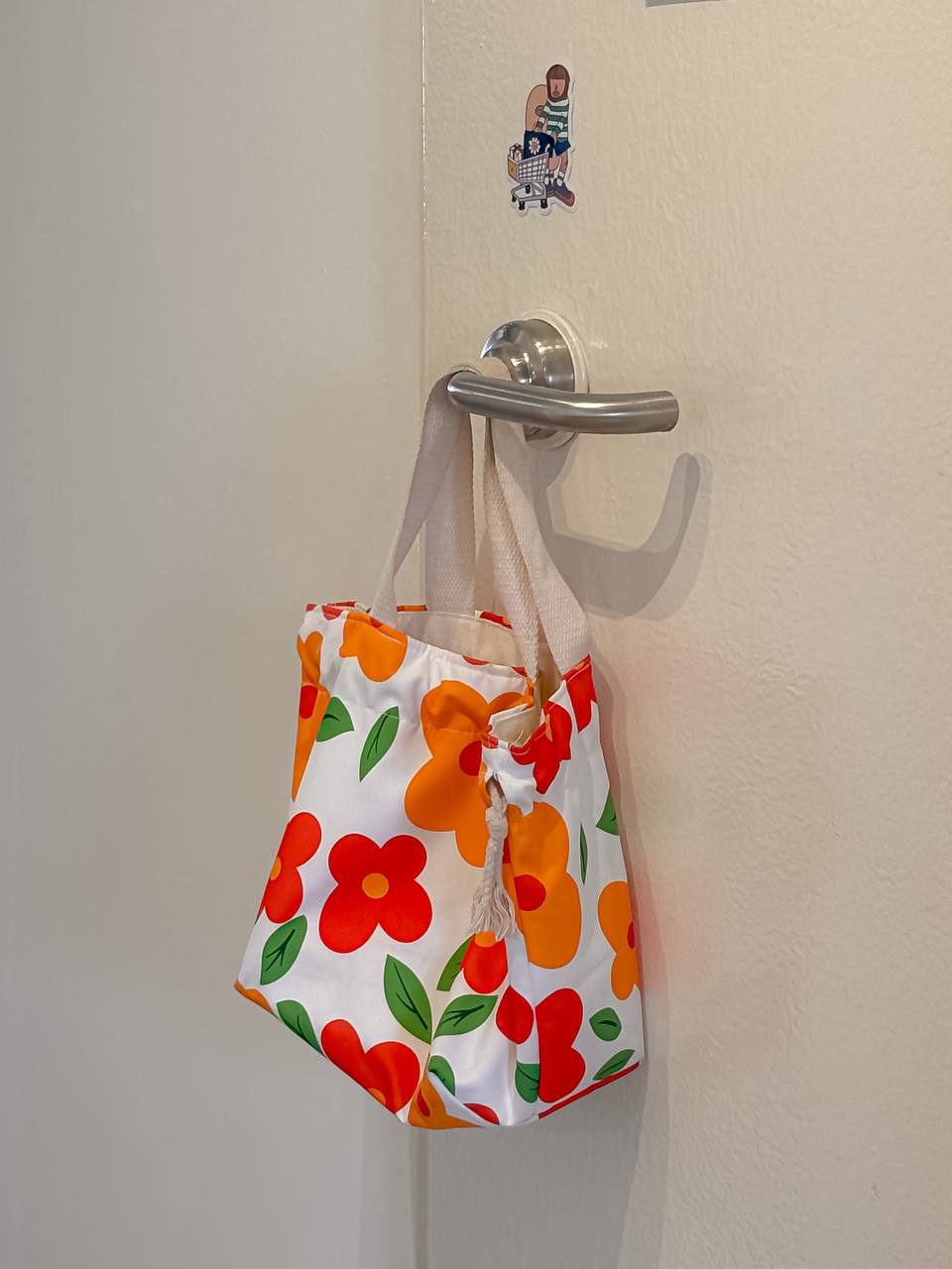 The Art in Our Home - Floral tote bag with vibrant red, orange, and green flowers, hanging on a metal hook, white background