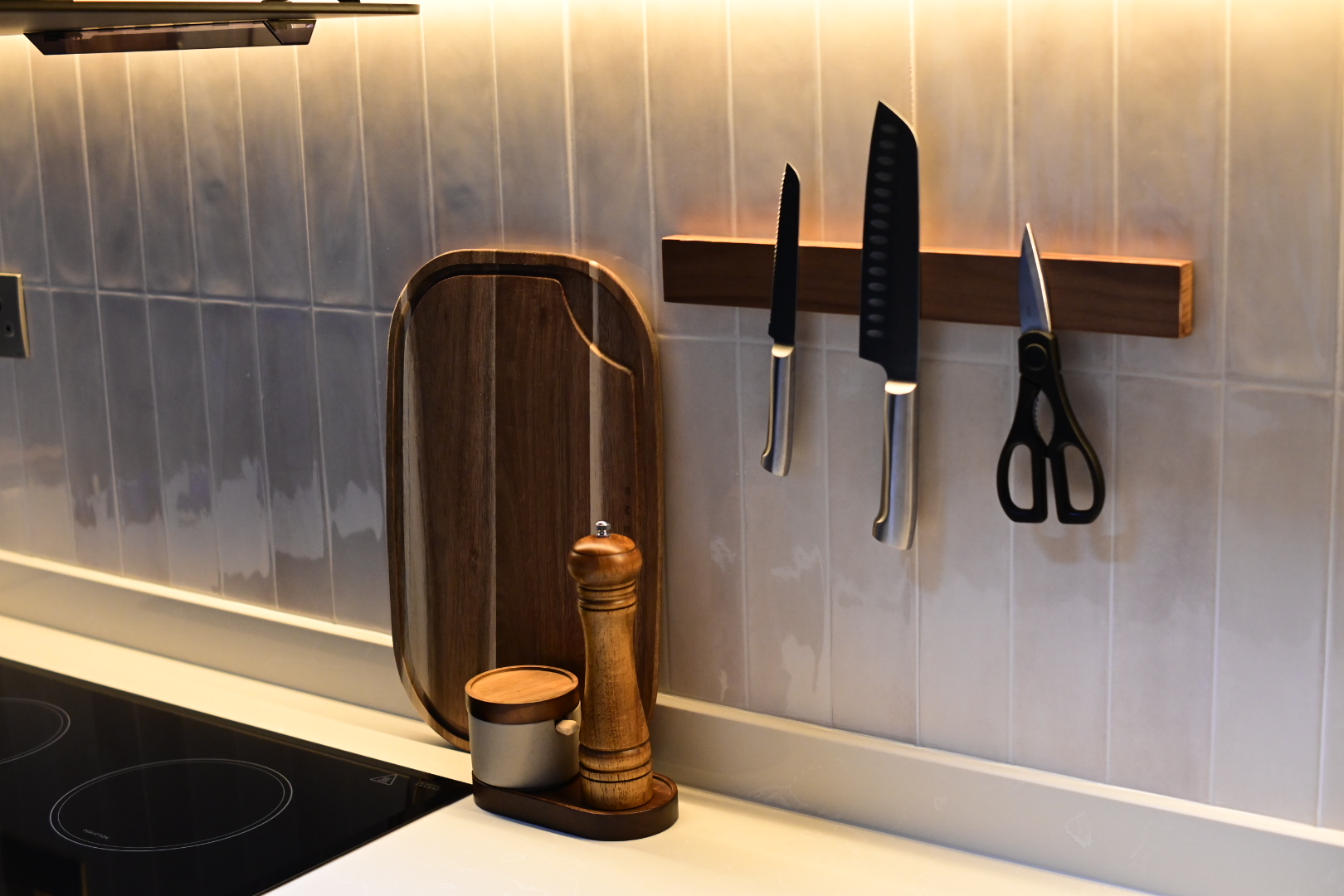 A functional closed kitchen space  - Wooden cutting board, black knife, black scissors, wooden spice grinder, white