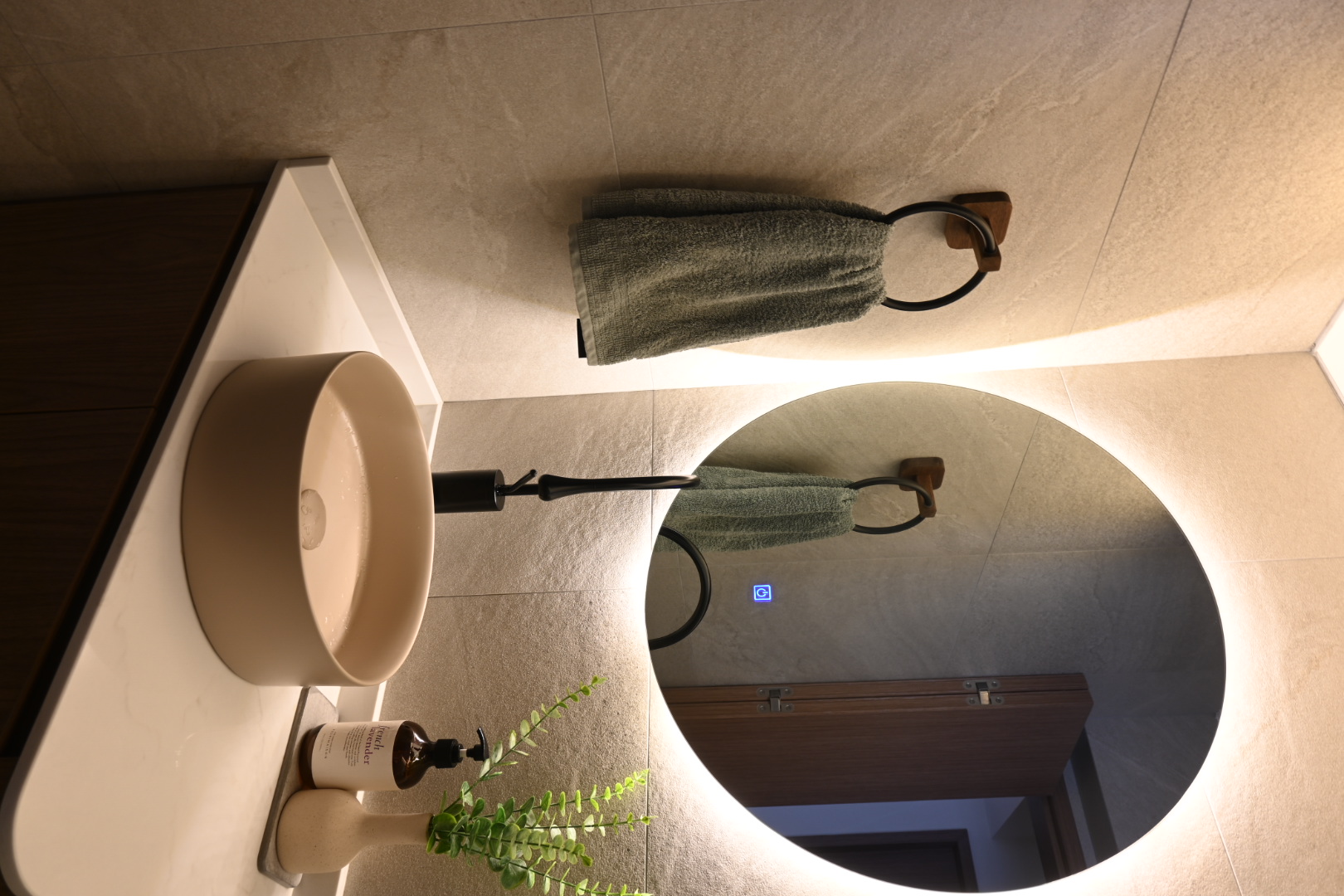 Bali inspired bathrooms  - Modern bathroom vanity, beige countertop, round mirror, green towel, wooden cabinet, plant in