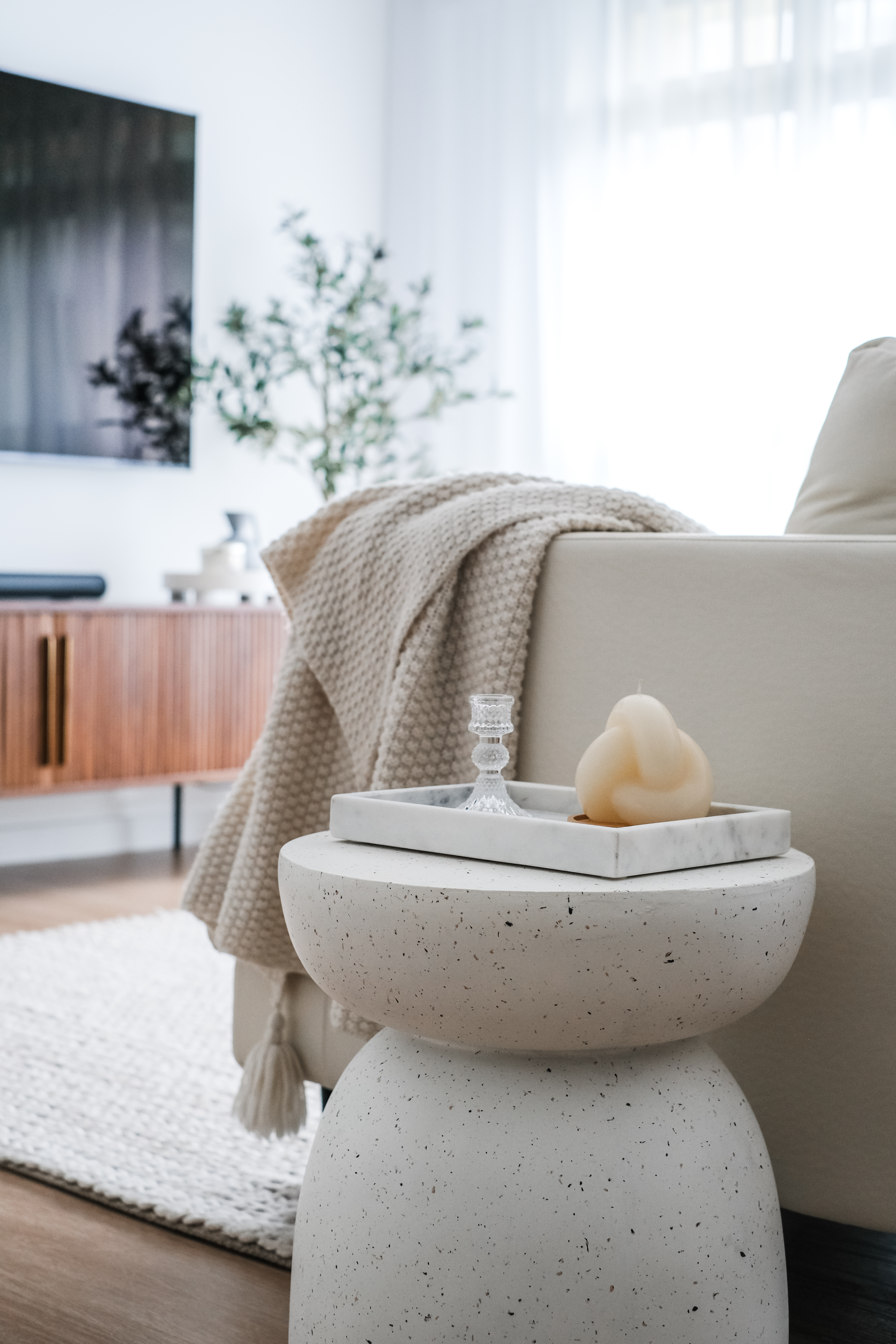 Modern Home With A Large Kitchen Island Around A Pillar. - Cream-colored knitted blanket, marble tray with candle, wooden