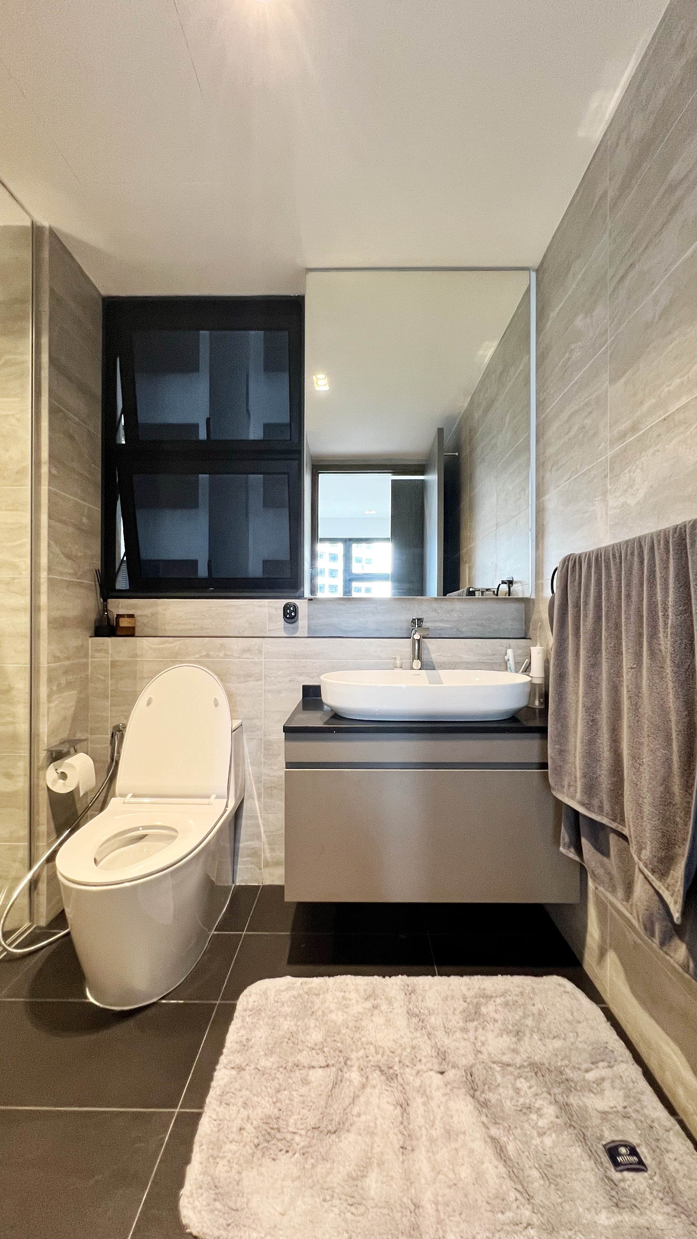 Our little cosmopolitan treehouse! - Modern bathroom with sleek design, gray and beige tiles, white toilet, large mirror