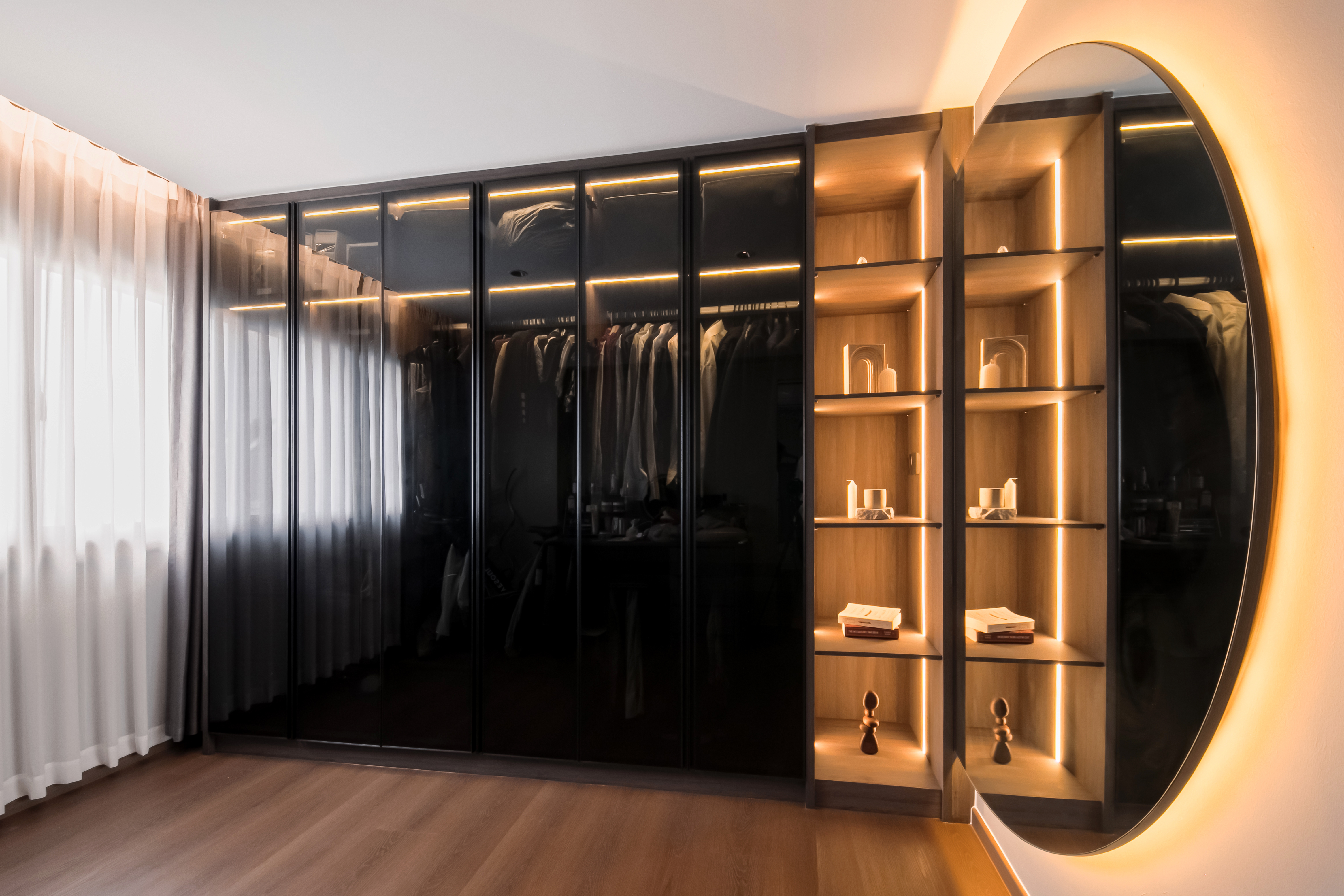 $120K Renovation for a Cozy & Warm Home - Modern wardrobe with sleek black doors, illuminated shelves, wooden interior, soft