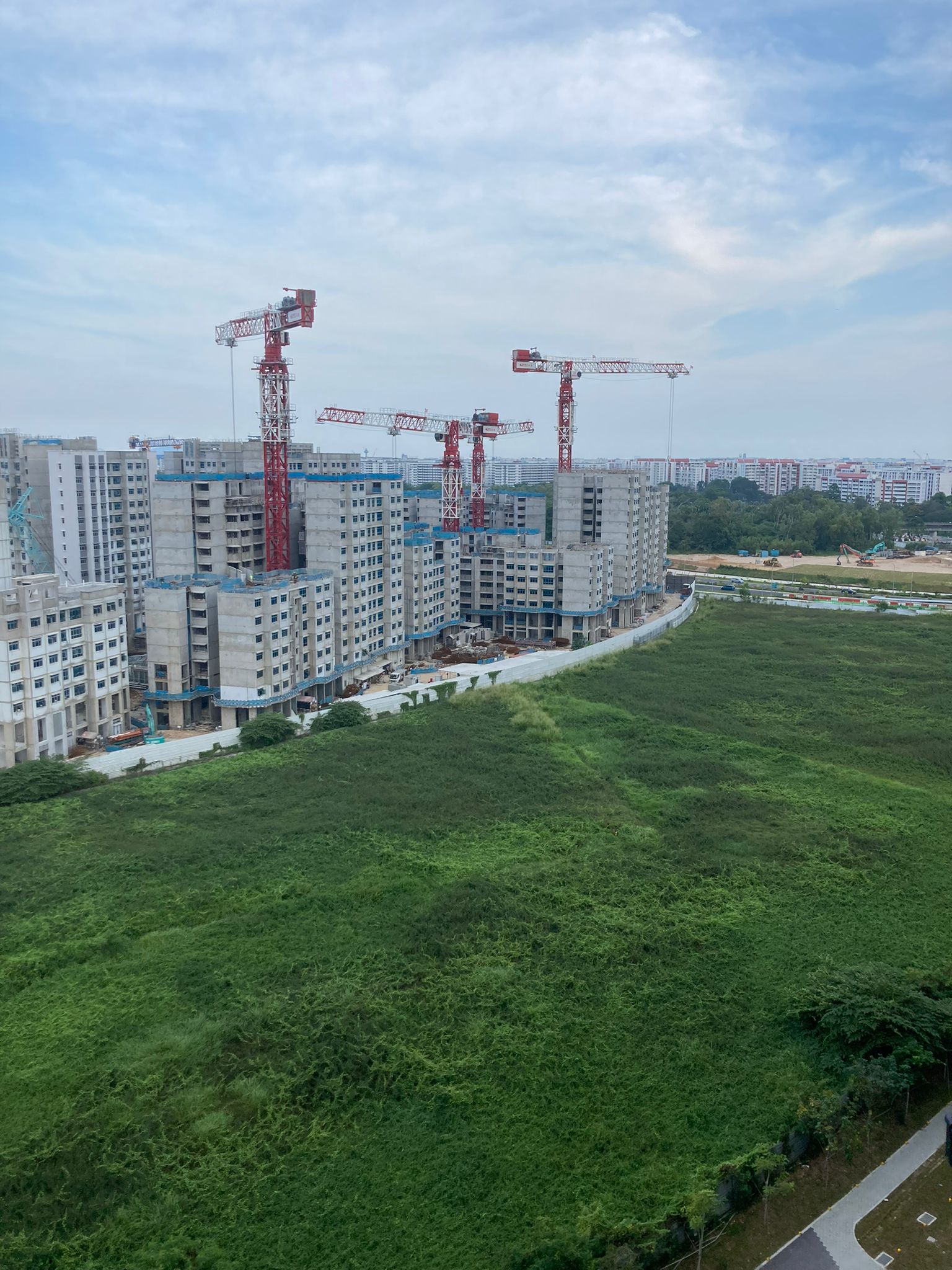 How we chose our BTO unit by elimination - Construction site with multiple cranes, green grass, and partially completed