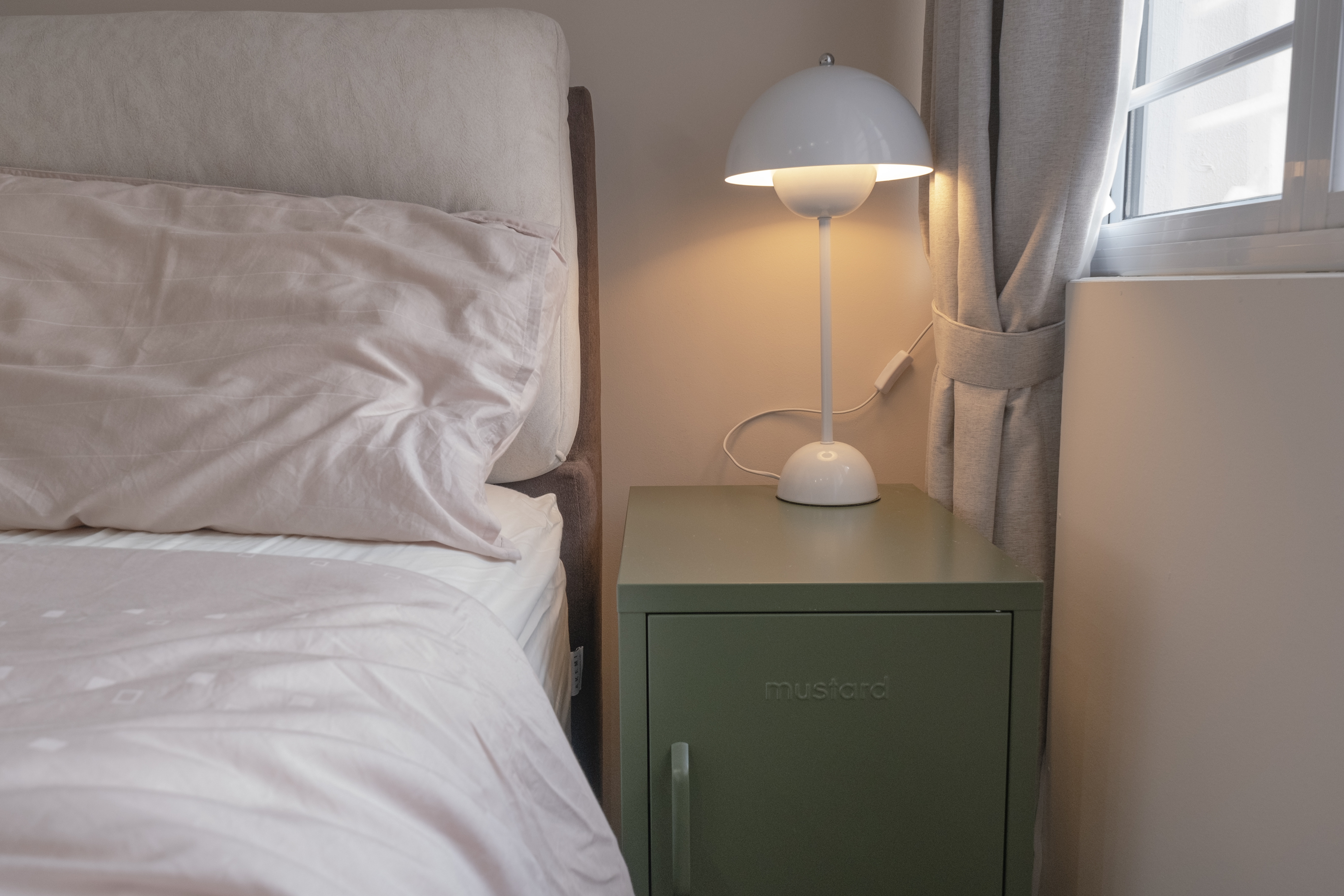 Inside our odd-shaped mid-century eclectic home - Bed, bedside table, green cabinet, white lamp, soft lighting, light beige