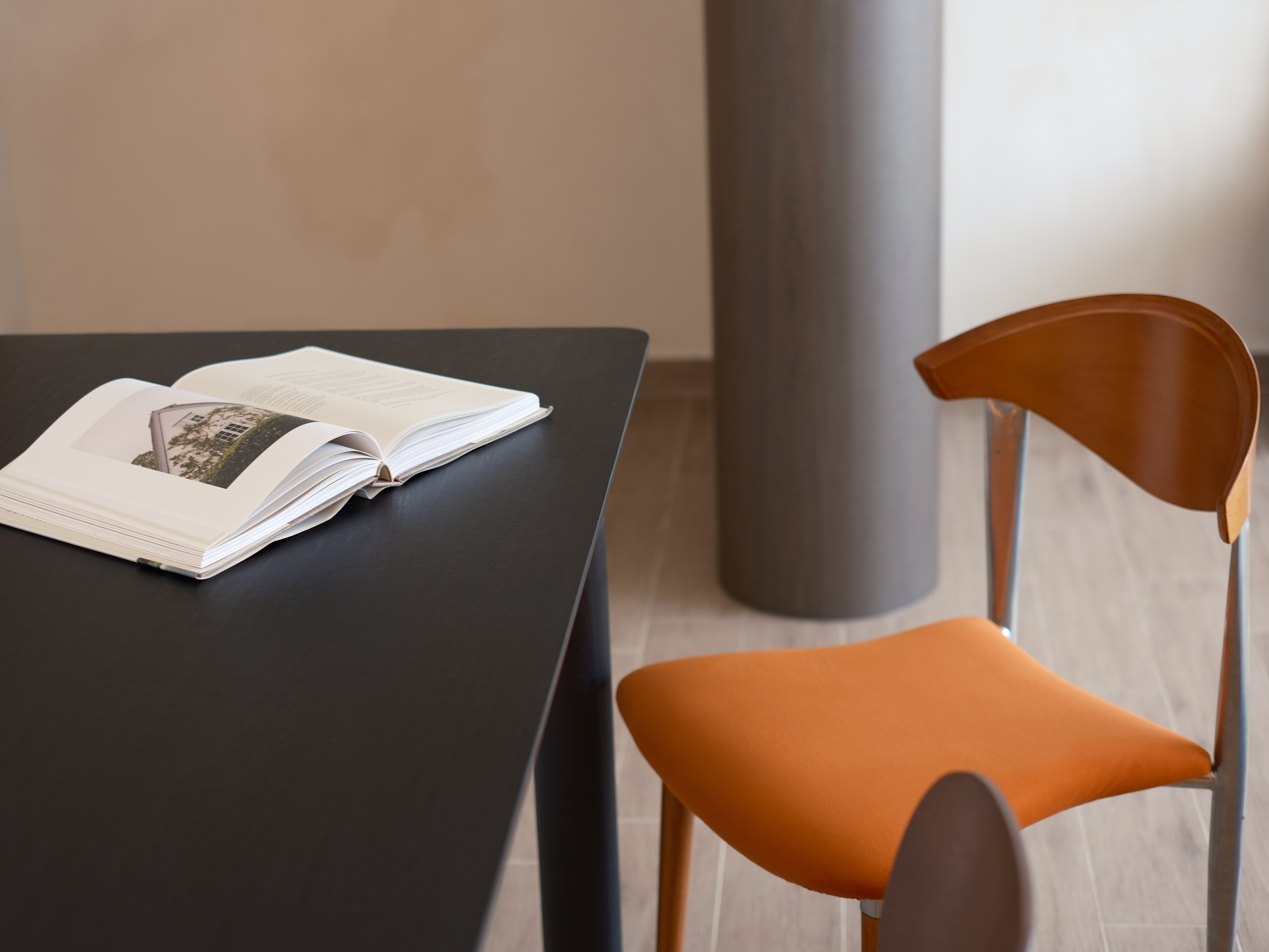 Embracing Minimalism in our Airy Dining Nook  - Open book with a photo of a house on the cover, black table, orange chair