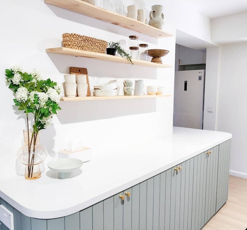 Renders vs. Reality: A Visual Journey - White kitchen island with light gray cabinets, wooden shelves displaying various