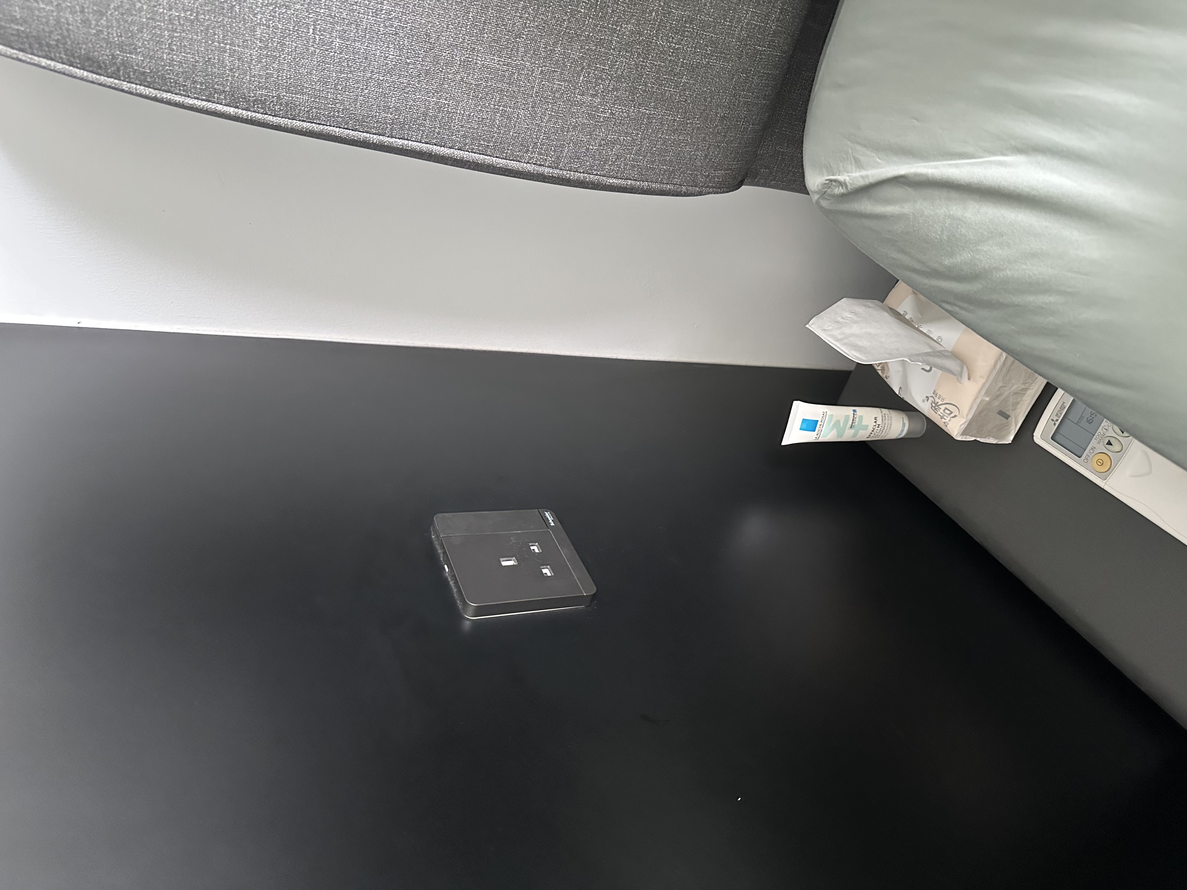 Dark and Muted Bedroom for Your Comfort! - Gray upholstered chair, black surface, small black device, white tube of cream