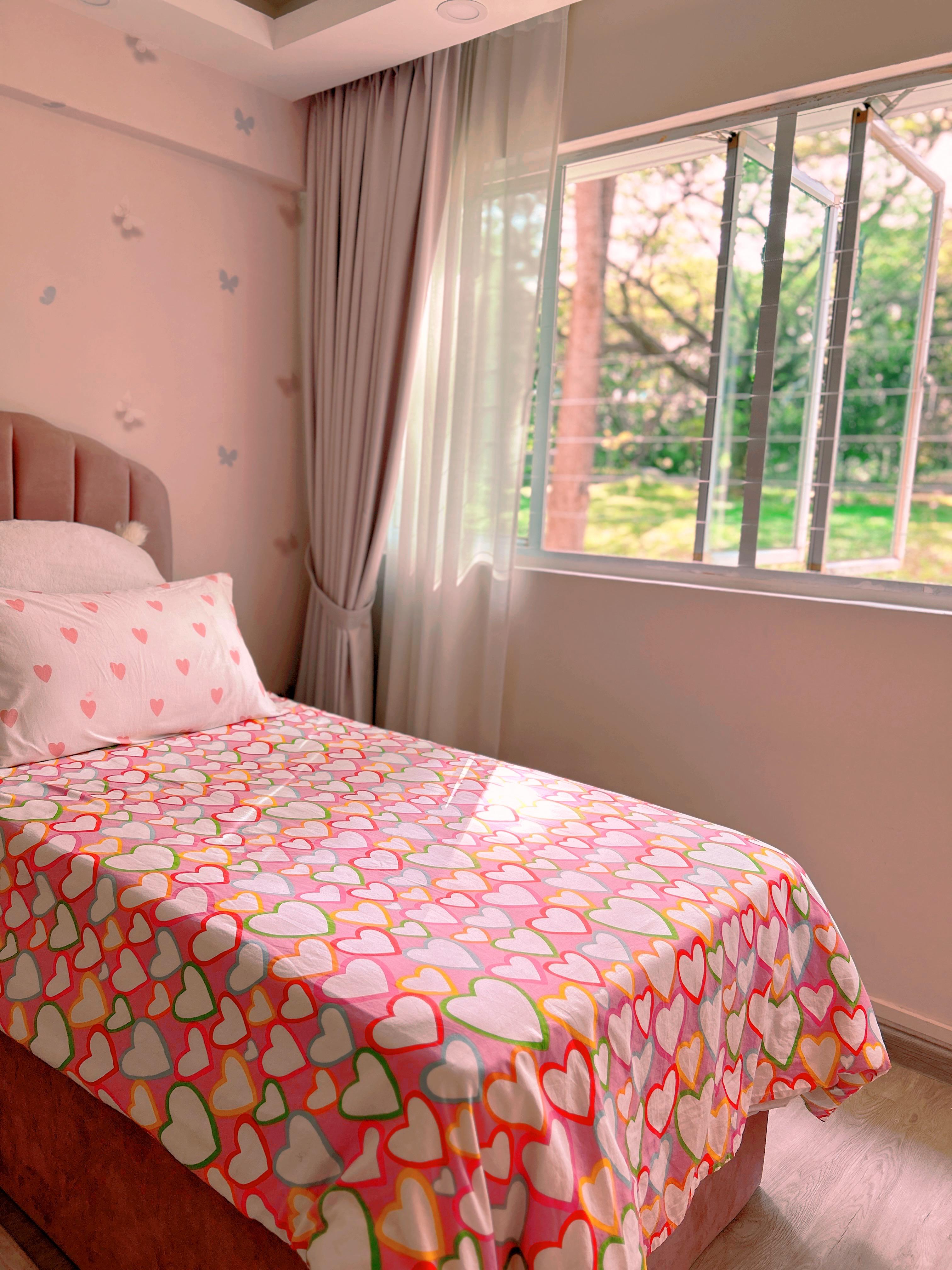 Pink Paradise: A Tour of Our Kids’ Dream Room! - Colorful heart-patterned bedspread, soft pink wall, white pillows, window