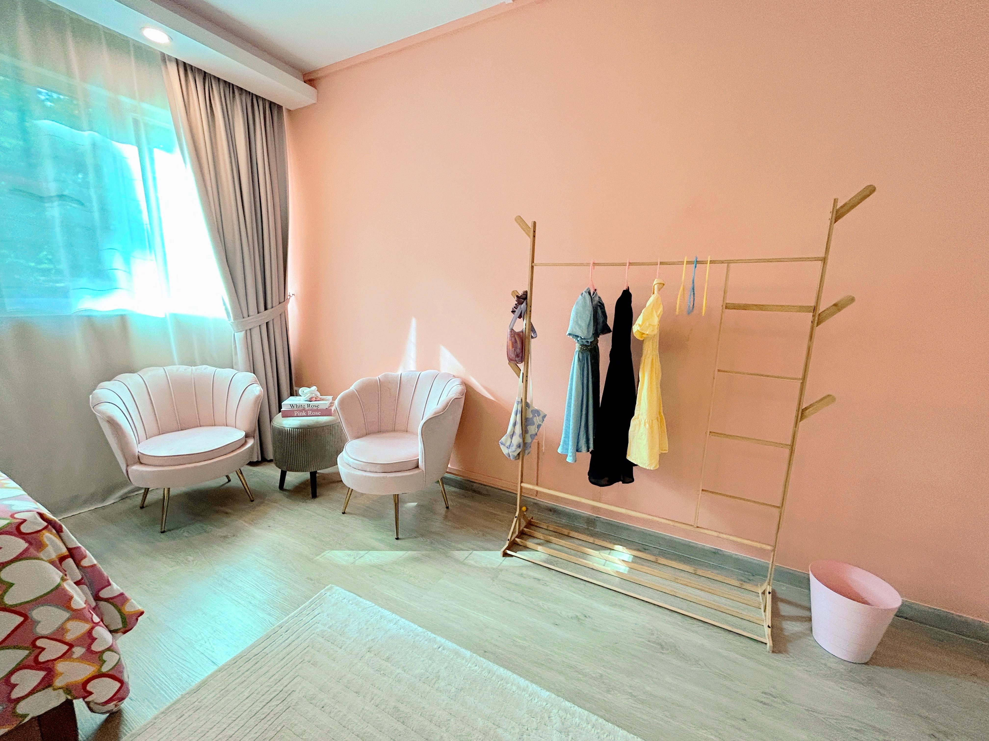 Pink Paradise: A Tour of Our Kids’ Dream Room! - Soft pastel pink walls, cozy armchair, wooden ladder shelf, colorful hanging