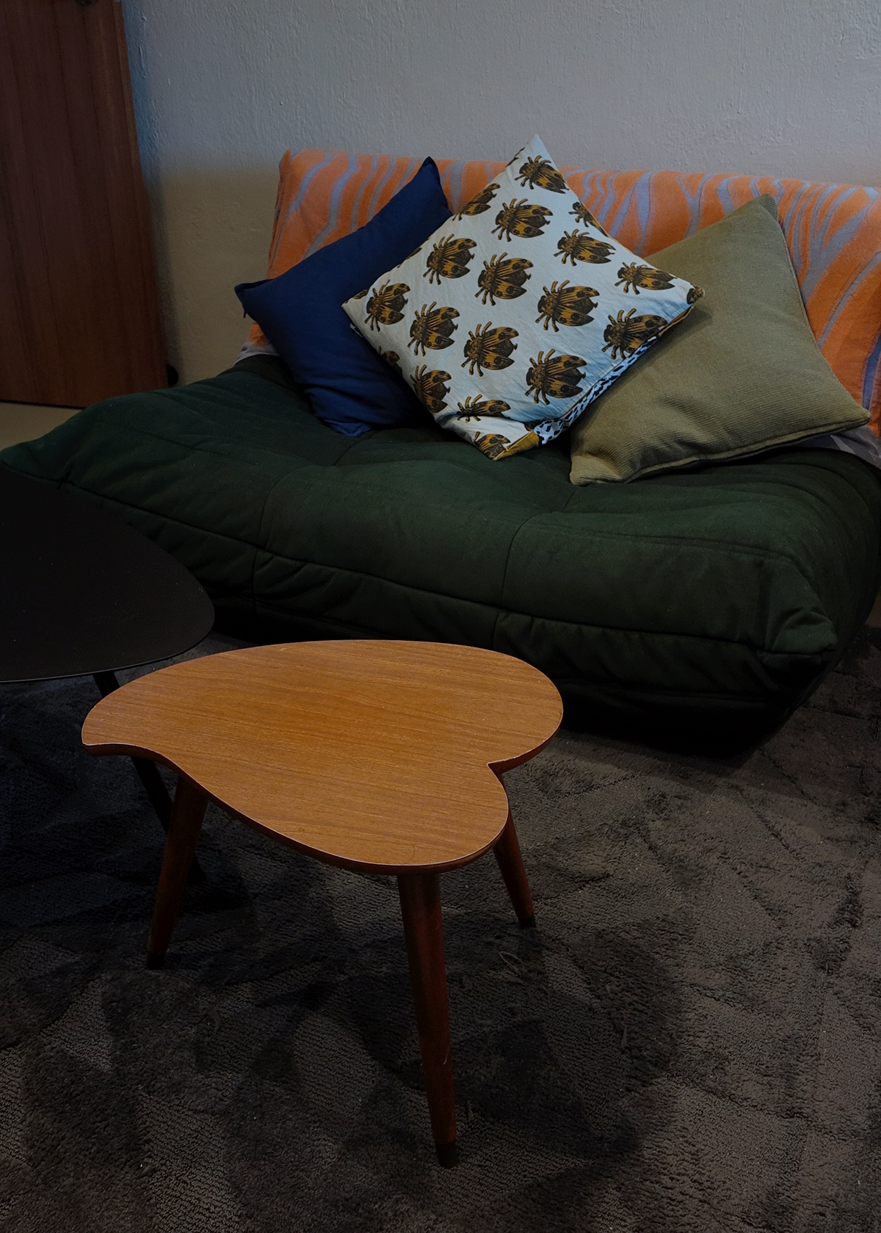 A living room within our bedroom - Couch with orange and blue striped cover, green pillow, patterned pillow, wooden coffee