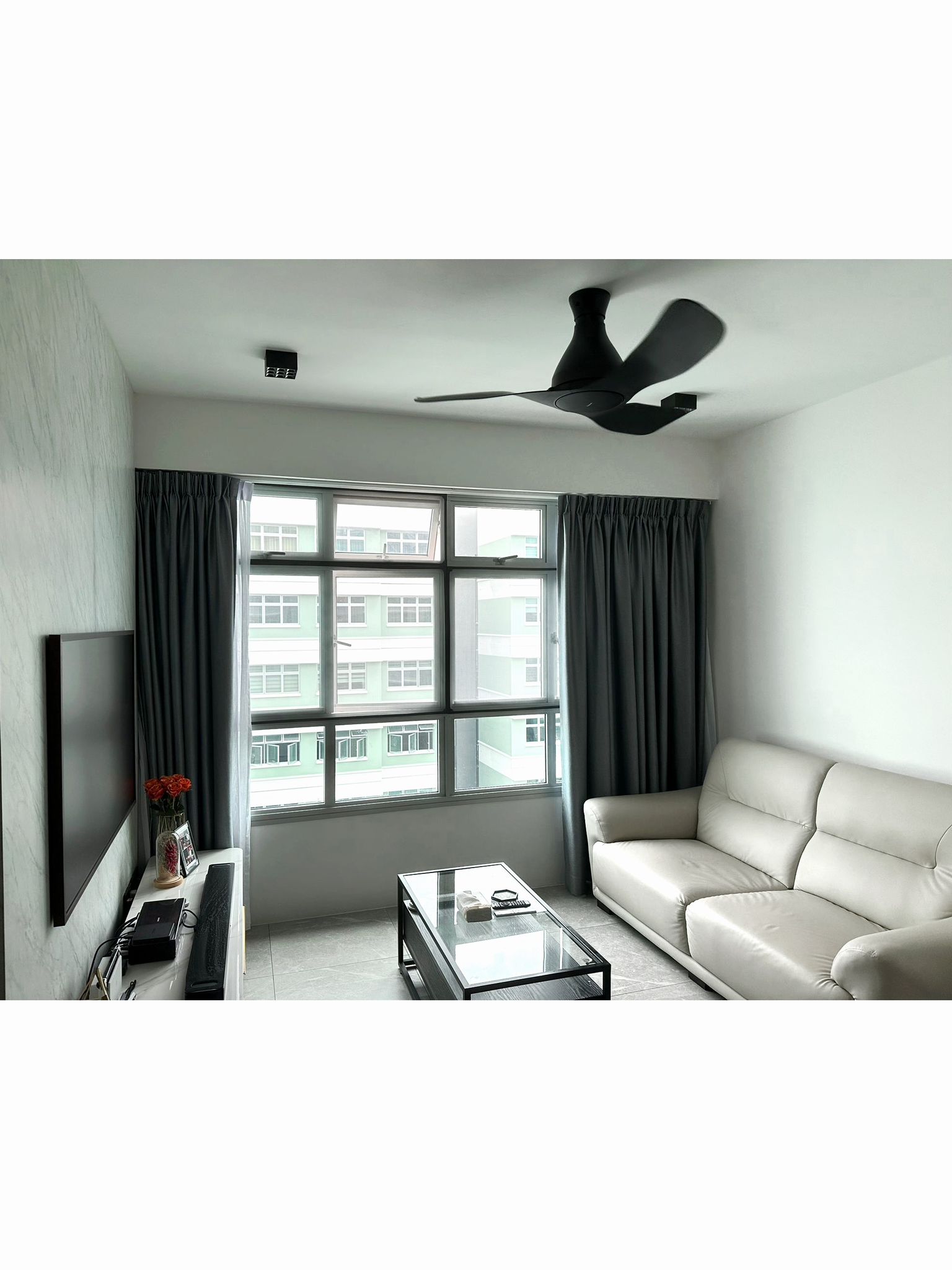 Living Room: neutral color palette, simple and neat. - Modern living room with large windows, beige sofa, black ceiling fan