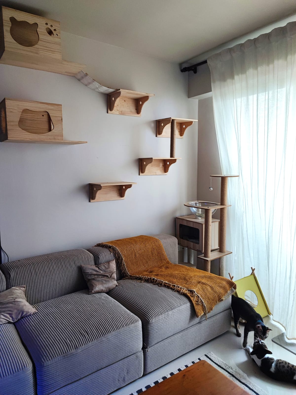 Purrfect Harmony: A living room for cats and their humans - Wooden cat tree, gray sofa, striped cushions, yellow blanket, cat
