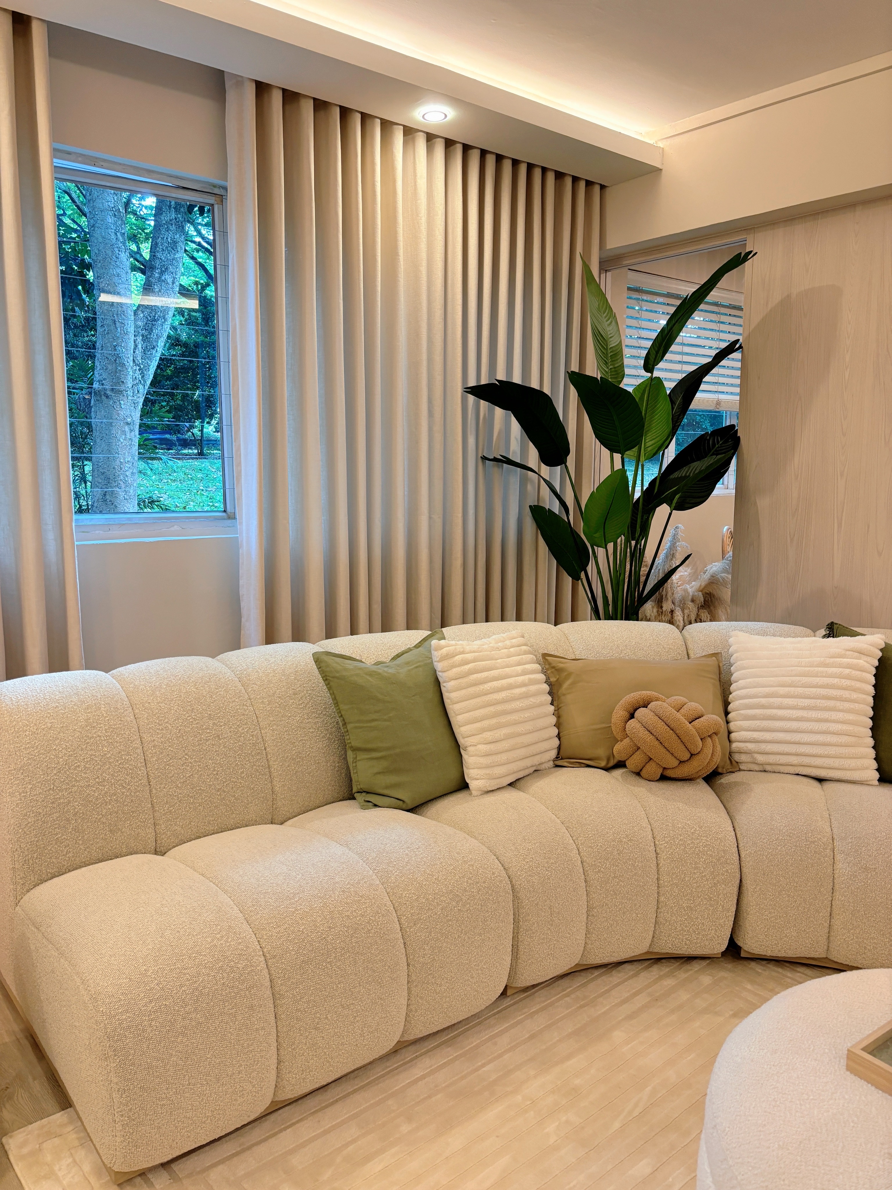 Sprucing Up Home Decor: Adding Greens for a Fresh Touch - Cream-colored sofa, beige curtains, large green plant, wooden