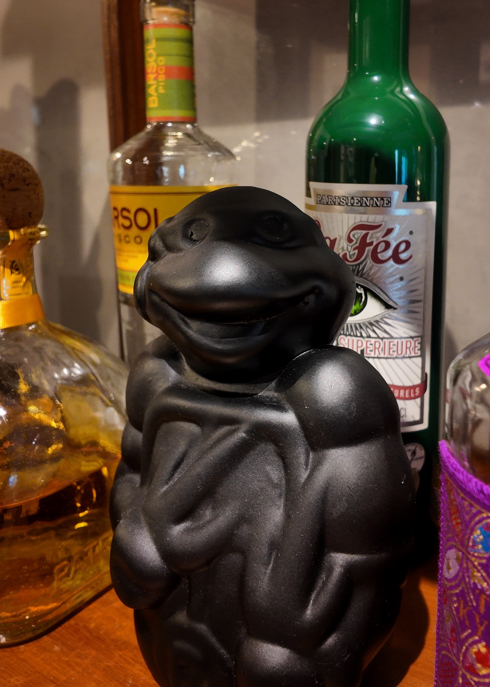 Enter this way folks! - Black sculpture with smiling face, Wooden shelf with various bottles, Distilled spirits in glass