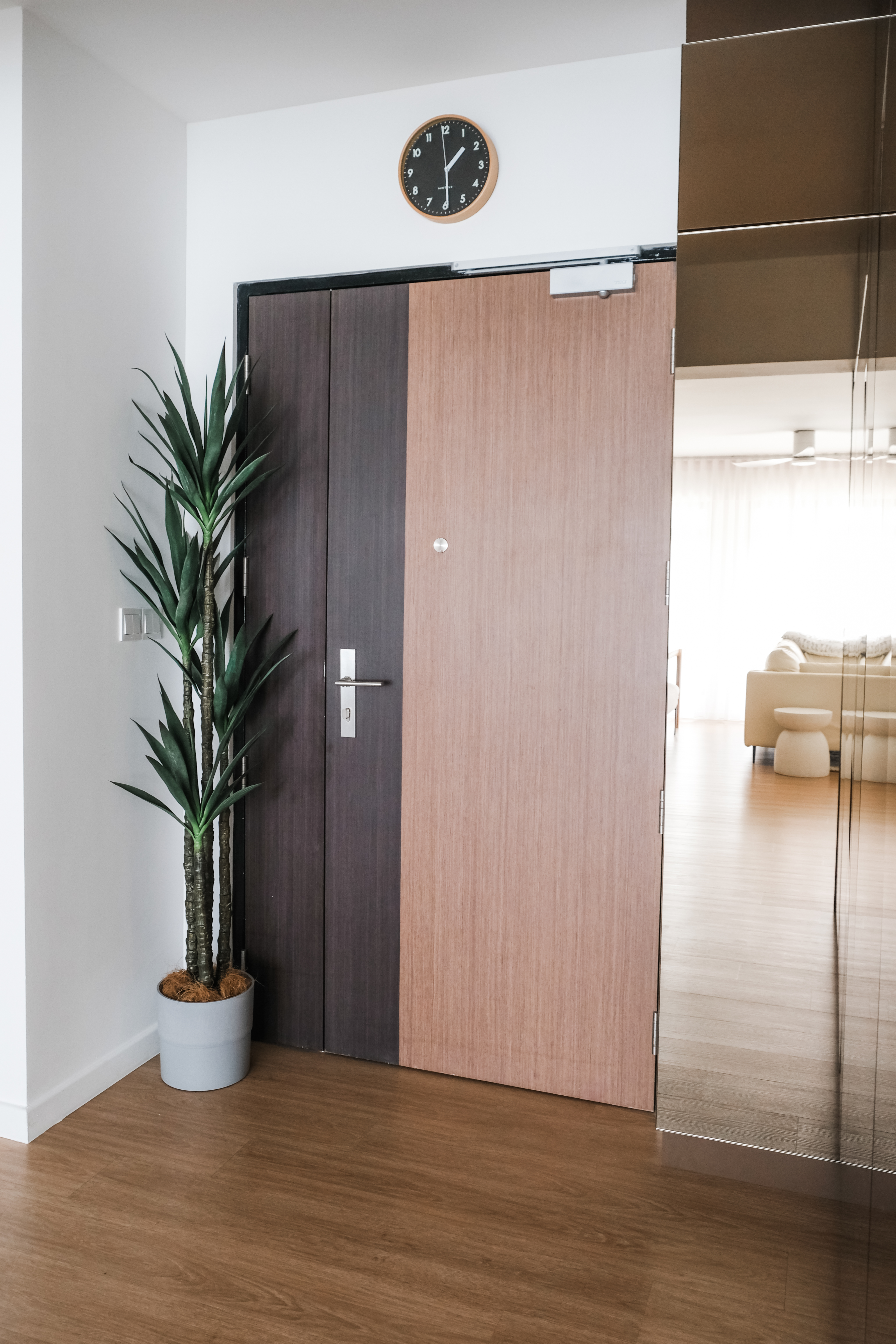 Inviting Entryway to a Spacious Open-Concept Home - Wooden door, modern interior, potted plant, clock on wall, minimalist