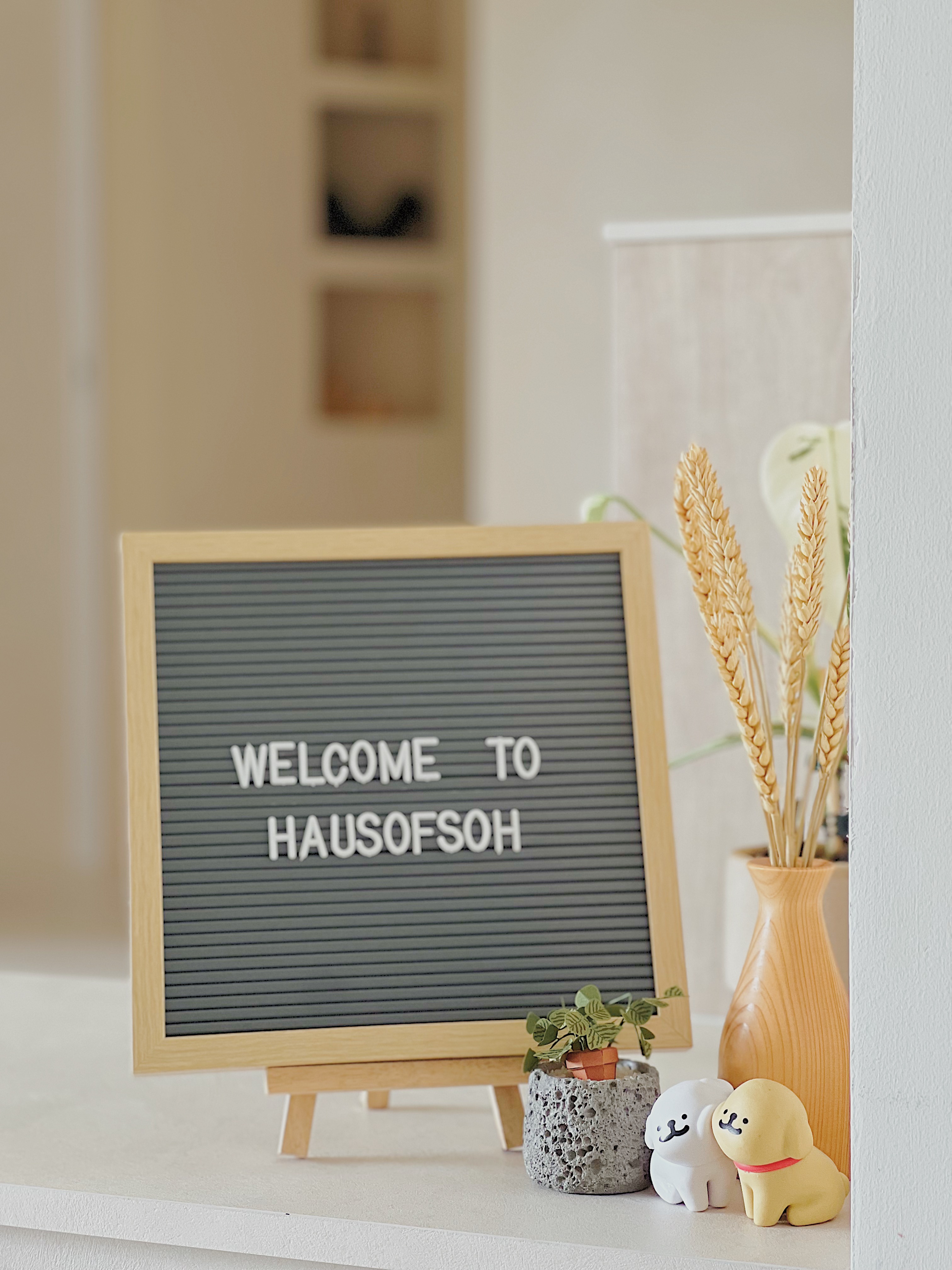 Welcome Home: Embracing Clutter-free Living - WELCOME TO, wooden easel, wheat stalks, potted plant, small ceramic dog