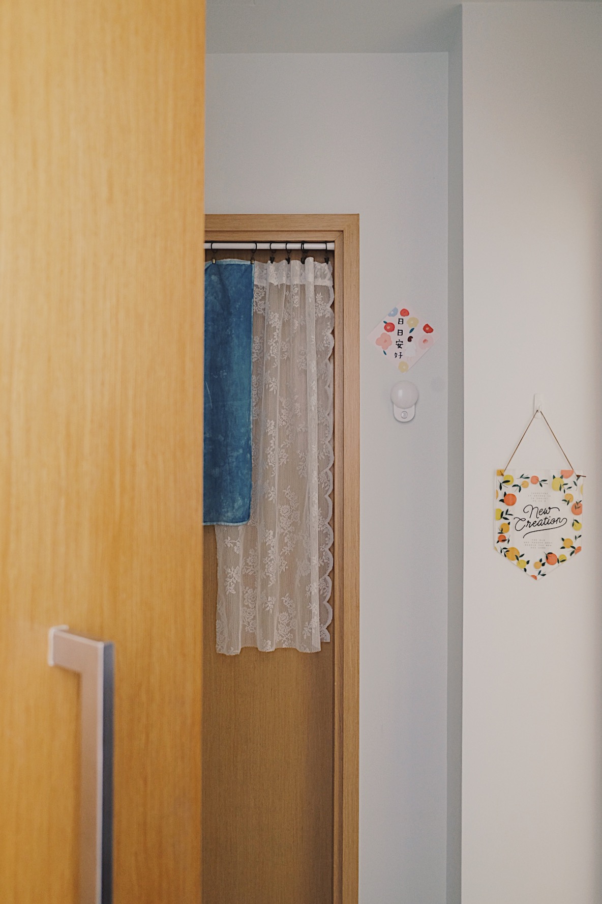 Cube-sized Foyer in a Dual-key Apt with a shoe rack and decor touches - Wooden door frame, blue towel, lace curtains, white