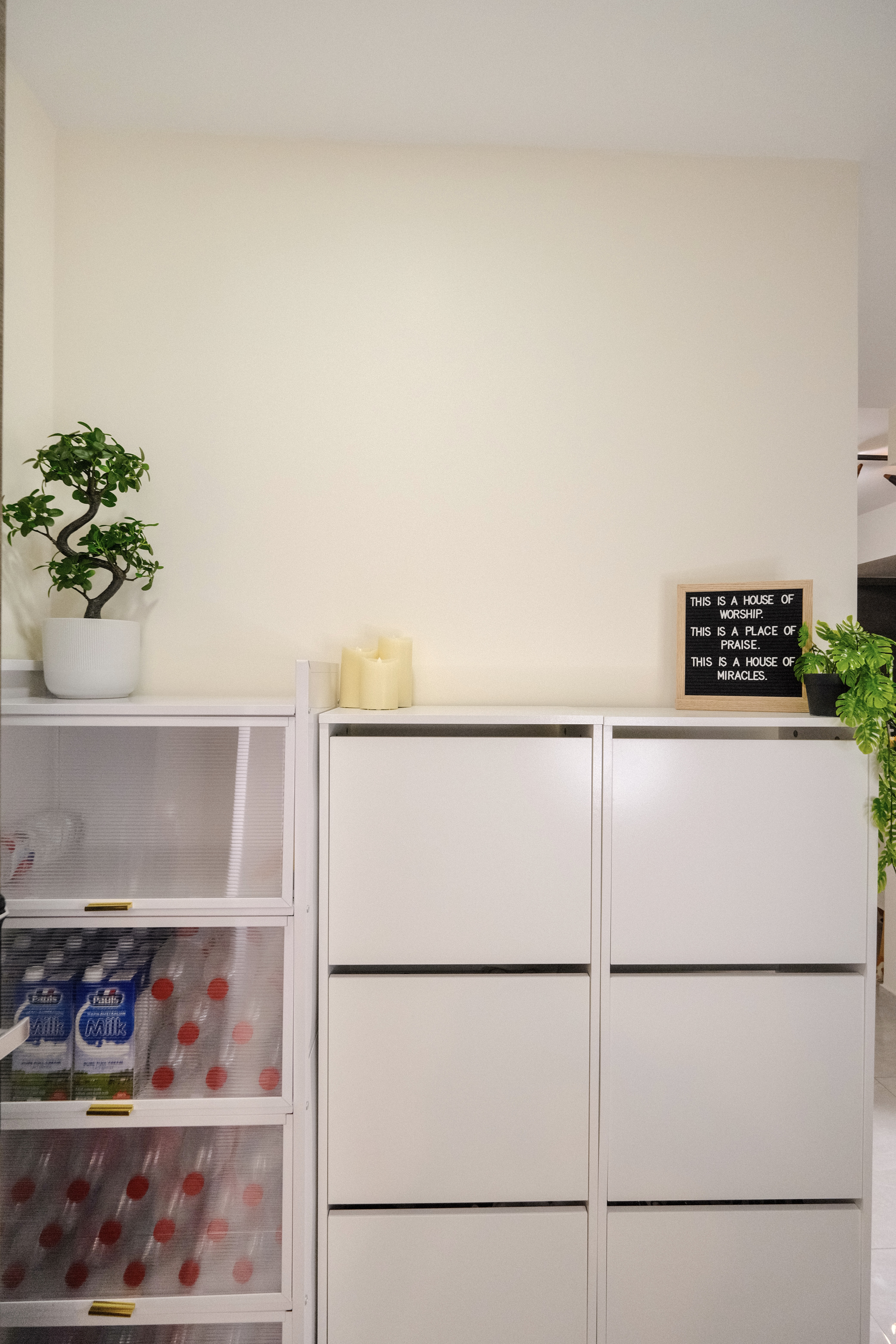 Step into our minimalist entryway!  - White minimalist kitchen cabinet, white drawers, potted plant, black chalkboard, "This