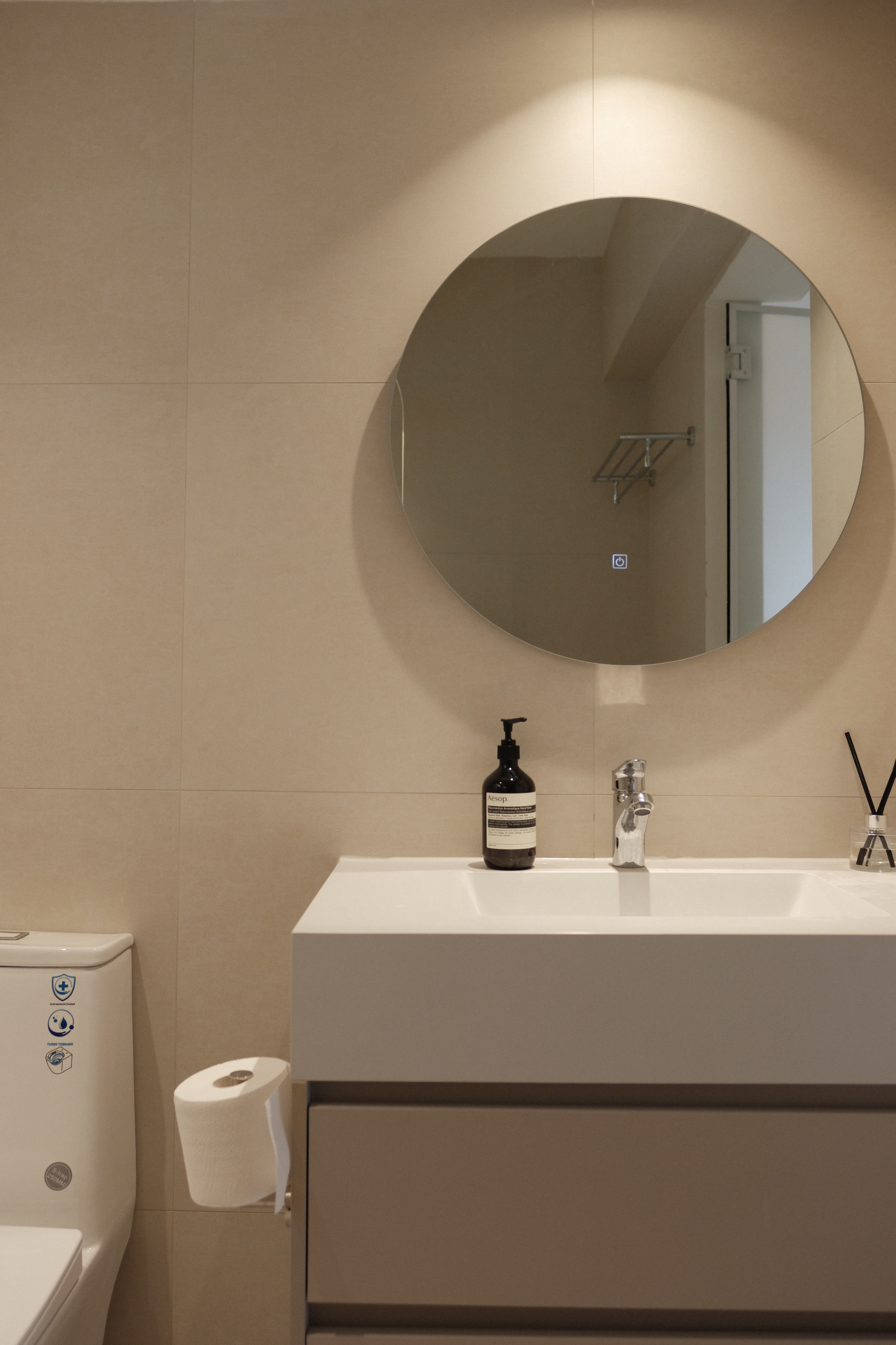 Creating A Soft Toned Master Bathroom - Round mirror, beige tiles, white sink, modern bathroom, toilet paper holder, soap