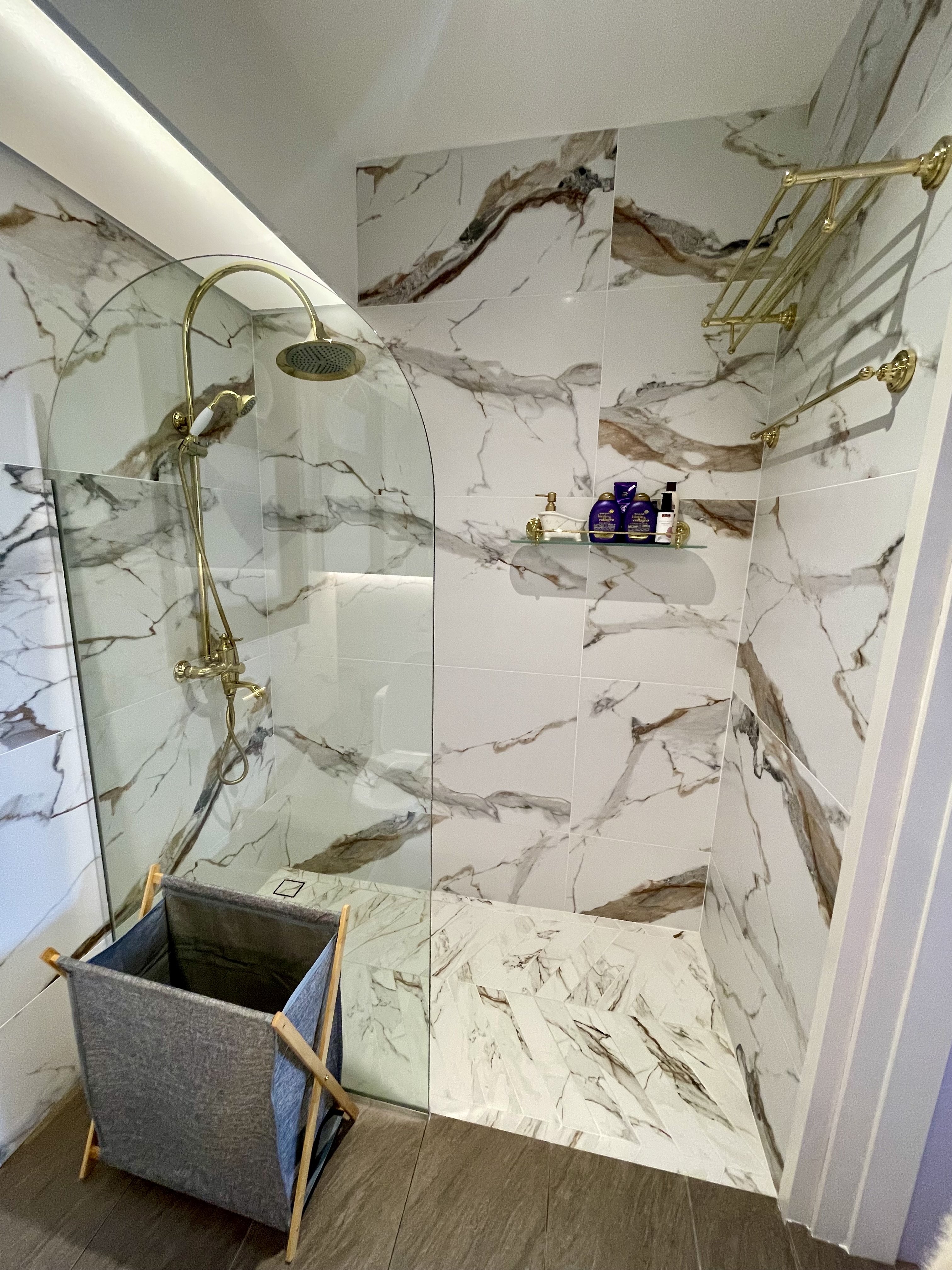 Our Bathroom Sanctuaries: A Concealed Luxe Master Ensuite VS Resort - Marble-patterned walls, glass shower enclosure, gold