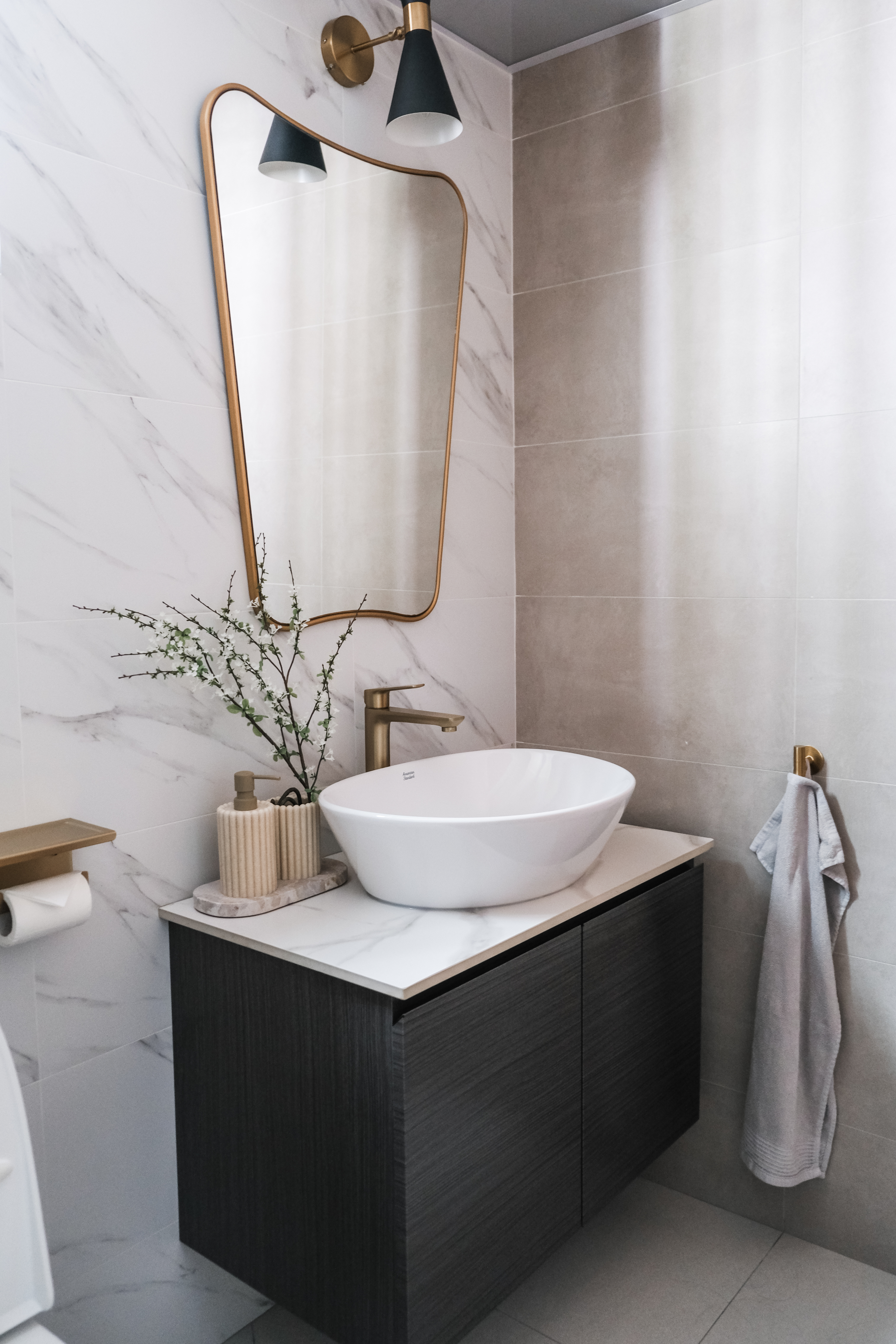 Sunlit Elegance: A Modern Bathroom Designed for Timeless Durability - White marble tiles, gold-framed mirror, modern bathroom
