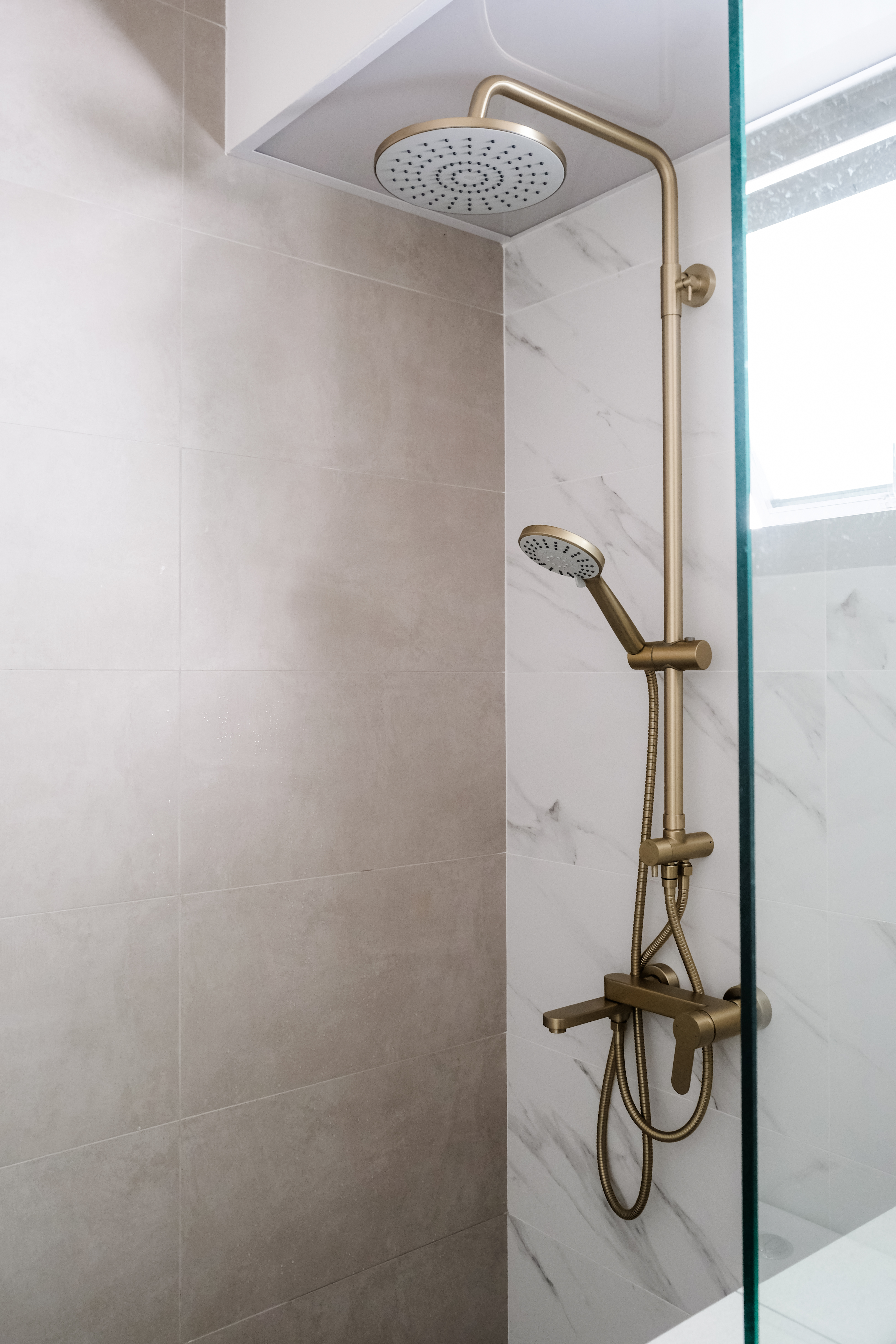 Sunlit Elegance: A Modern Bathroom Designed for Timeless Durability - Golden shower head and hose, marble tiles, modern