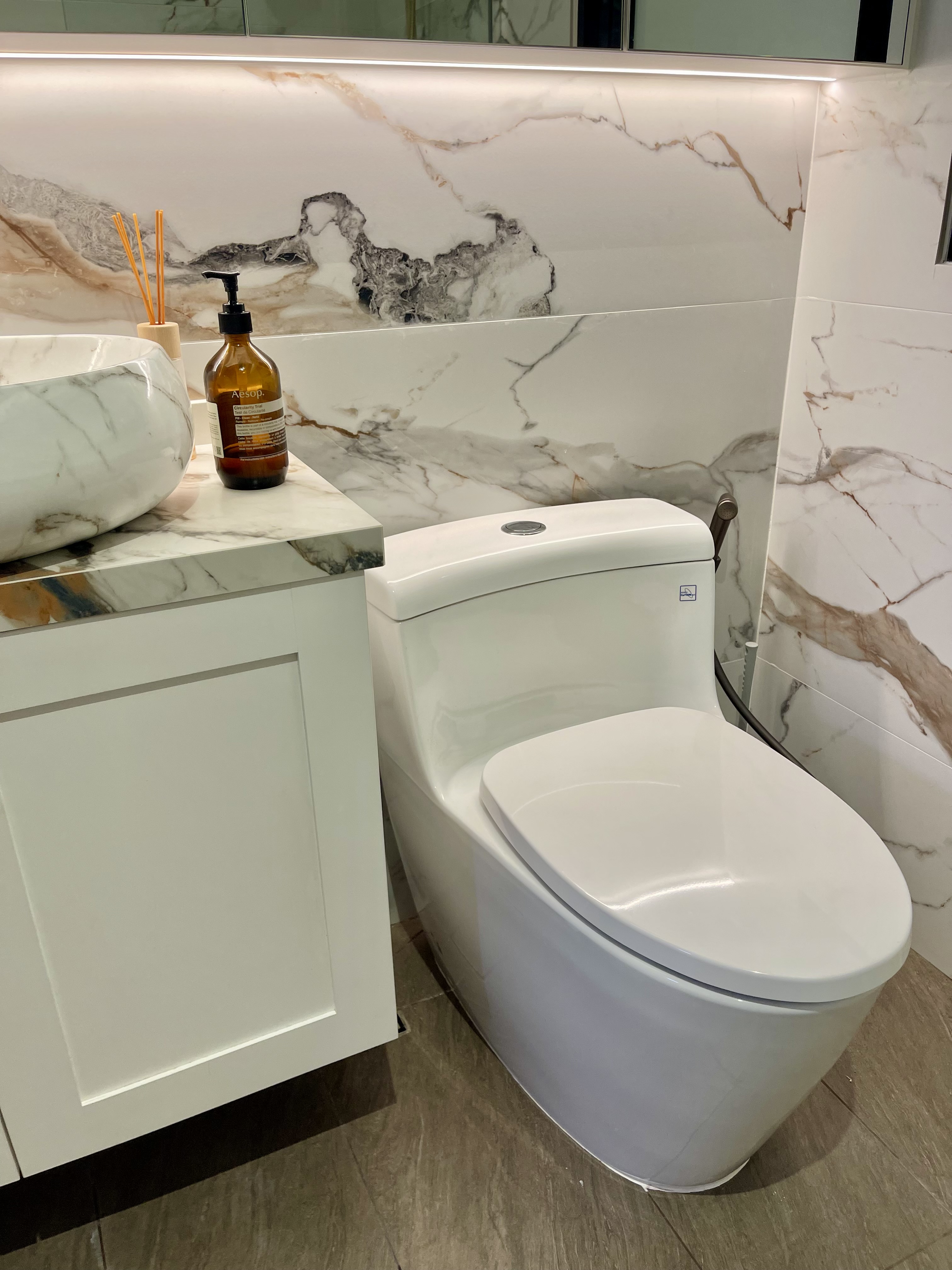 Our Bathroom Sanctuaries: A Concealed Luxe Master Ensuite VS Resort - Marble-patterned bathroom vanity, modern toilet, white