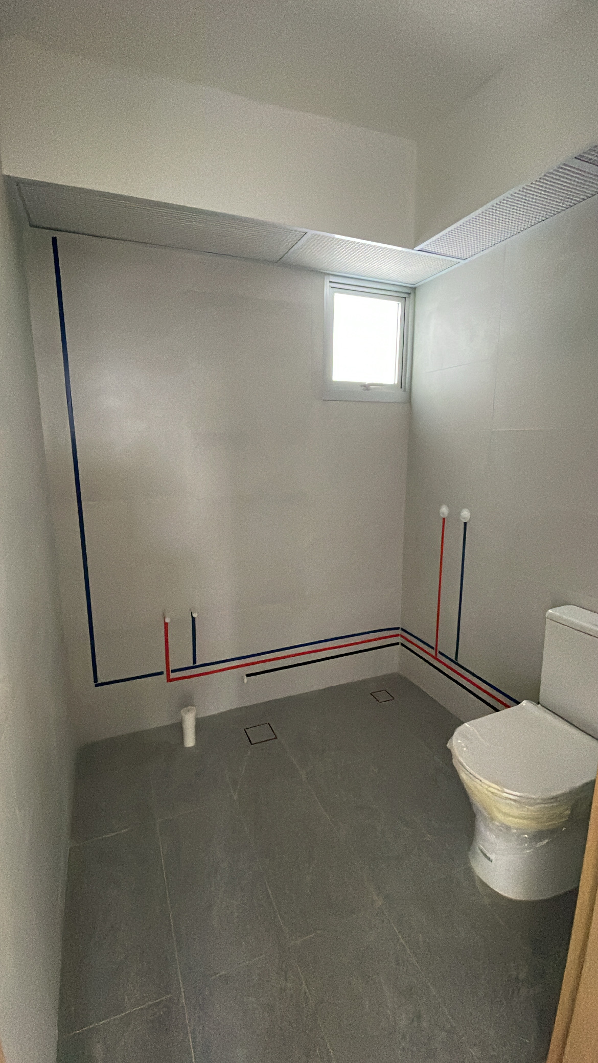 Elevate Your Space: Hotel-Inspired Bathrooms Transformation - White bathroom with gray tiles, red and blue piping, unfinished