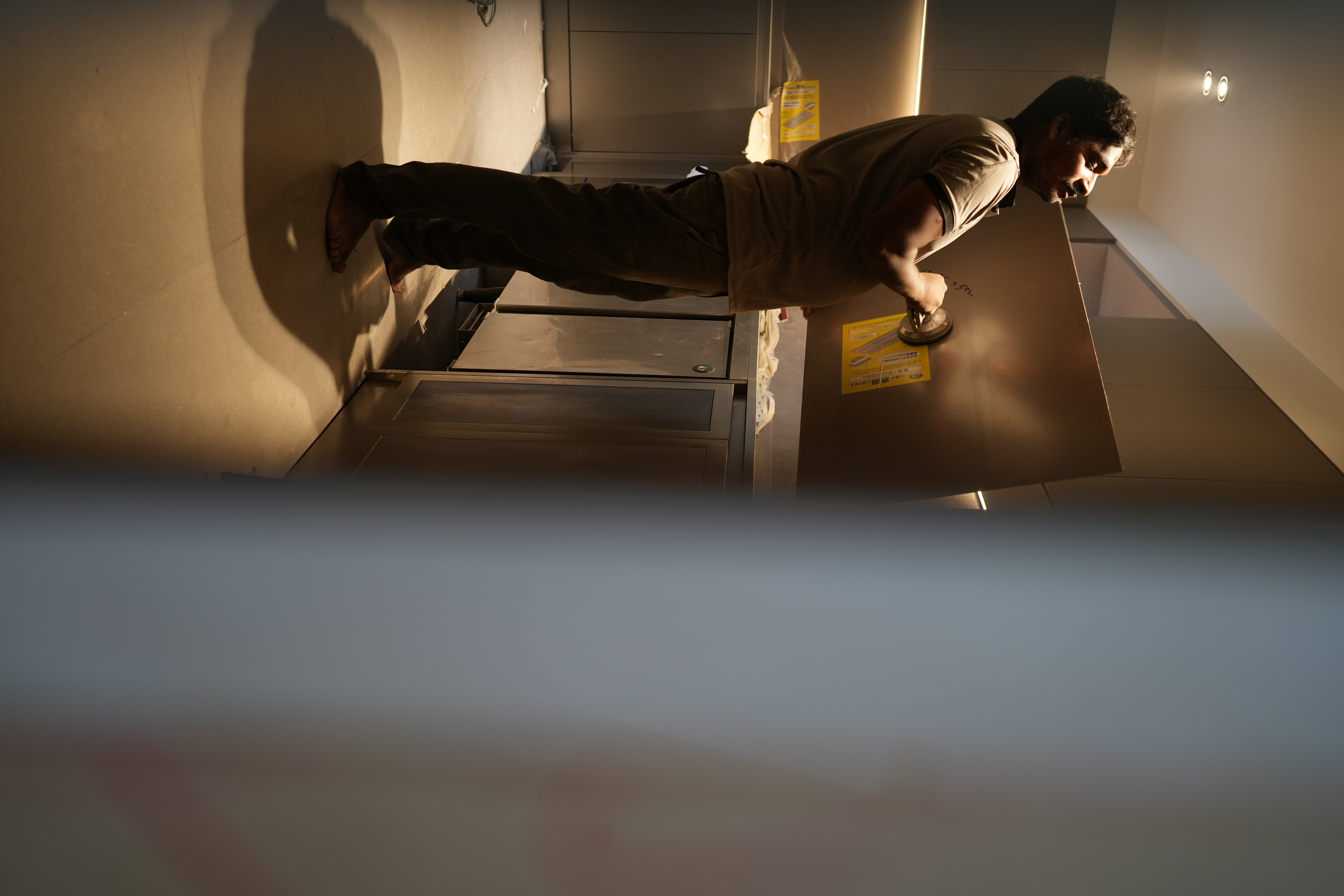 FAQ with @hitotema.home - dimly lit room, man leaning on wall, barefoot, dark pants, metallic surface, yellow warning signs