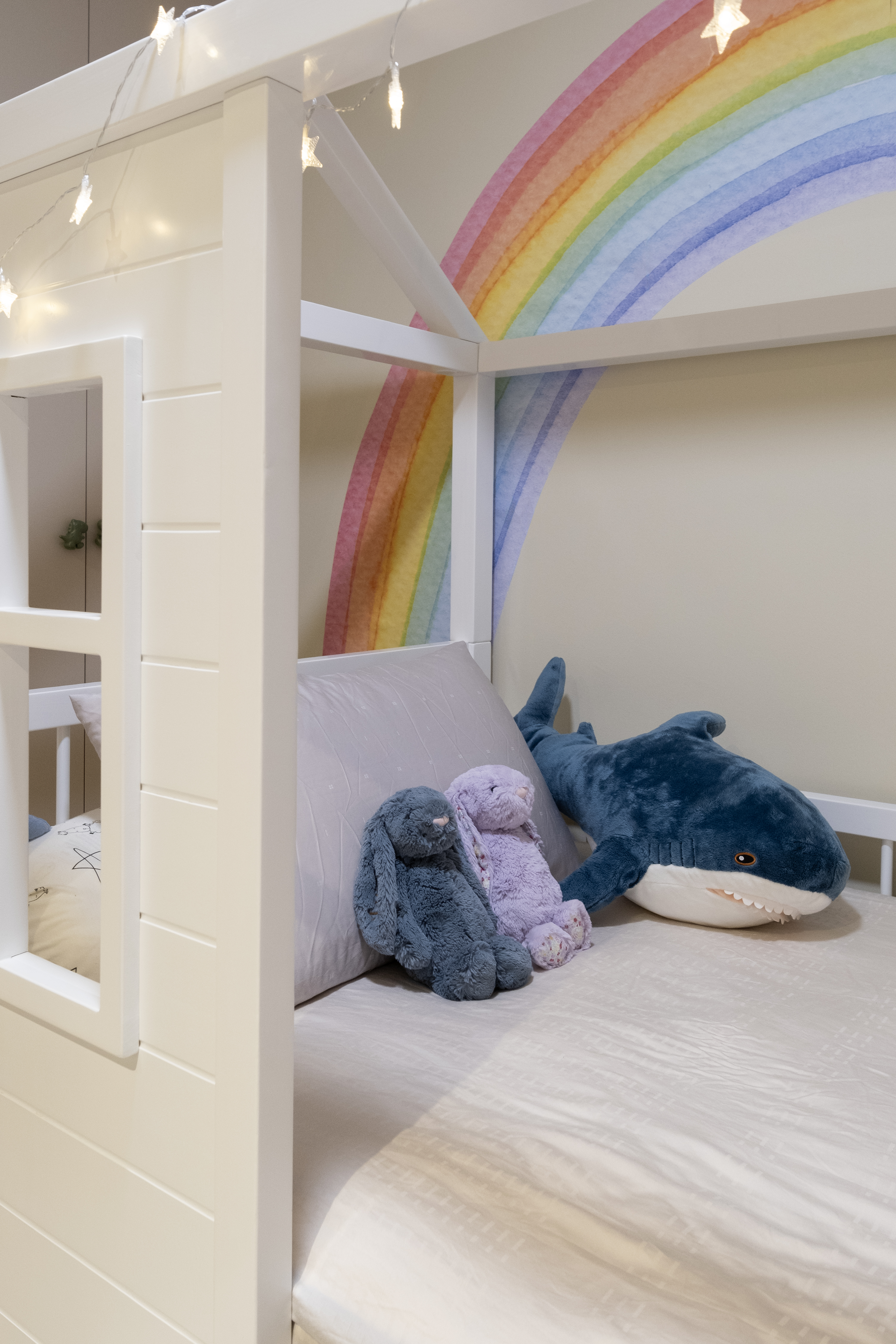 Whimsical Pastel Rainbow & Dino-Themed Kids’ Room - White bunk bed with soft bedding, plush toys, rainbow wall art, fairy